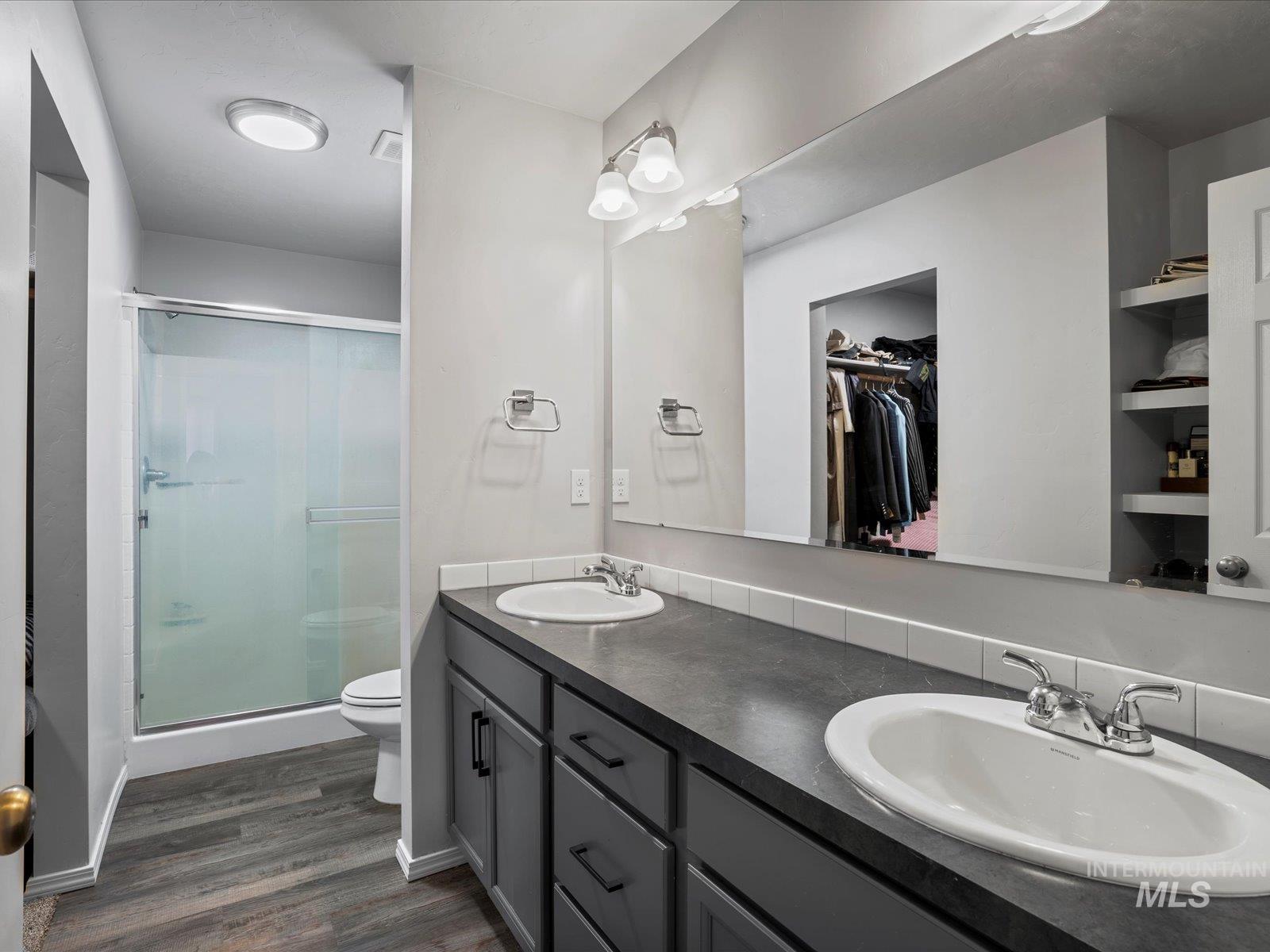 Full bath featuring a stall shower, wood finished floors, double vanity, and a spacious closet