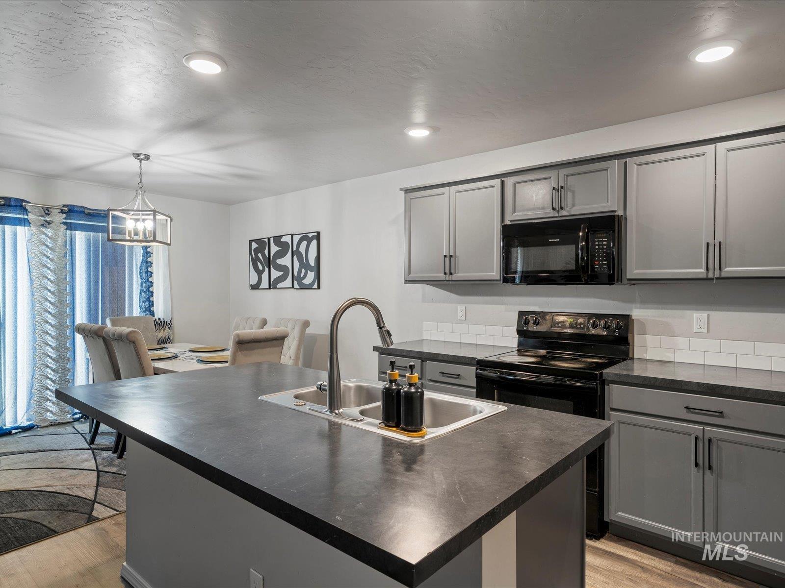 Kitchen with black appliances, dark countertops, gray cabinetry, light wood-style floors, and a kitchen island with sink