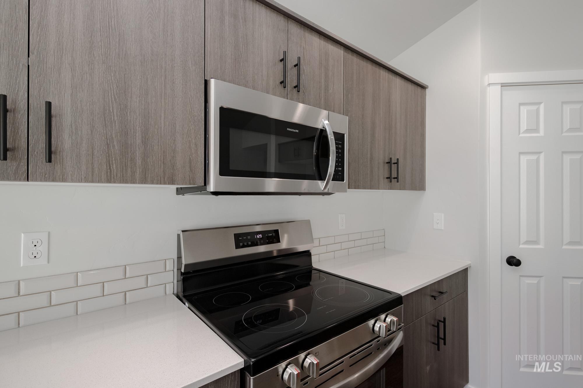 Kitchen featuring stainless steel appliances, modern cabinets, decorative backsplash, and light stone counters