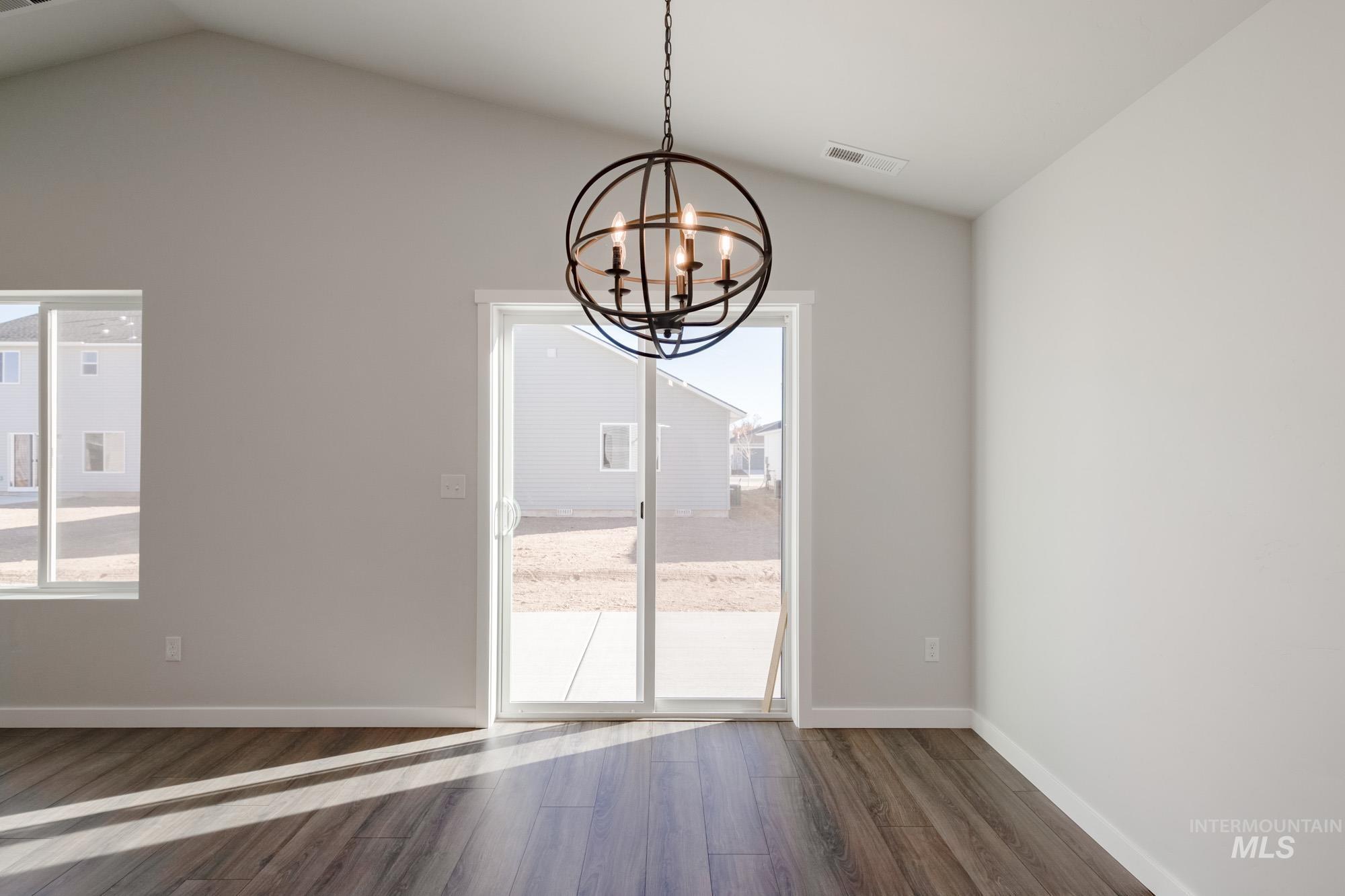 Unfurnished dining area featuring dark wood finished floors, lofted ceiling, and a chandelier