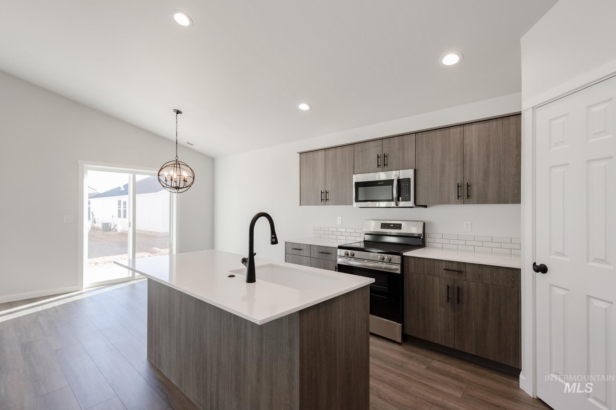 Kitchen featuring appliances with stainless steel finishes, decorative light fixtures, a center island with sink, dark wood-style floors, and lofted ceiling