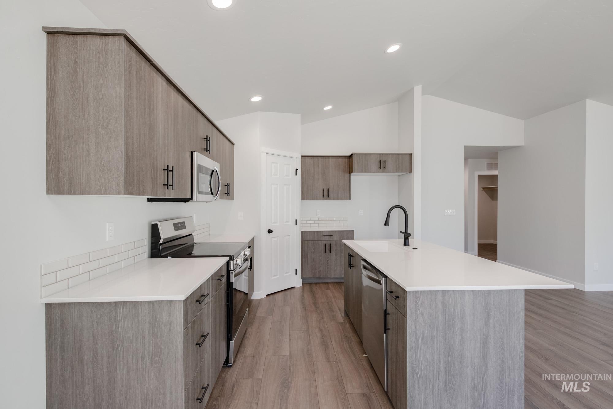 Kitchen featuring appliances with stainless steel finishes, modern cabinets, light wood-style floors, lofted ceiling, and a kitchen island with sink