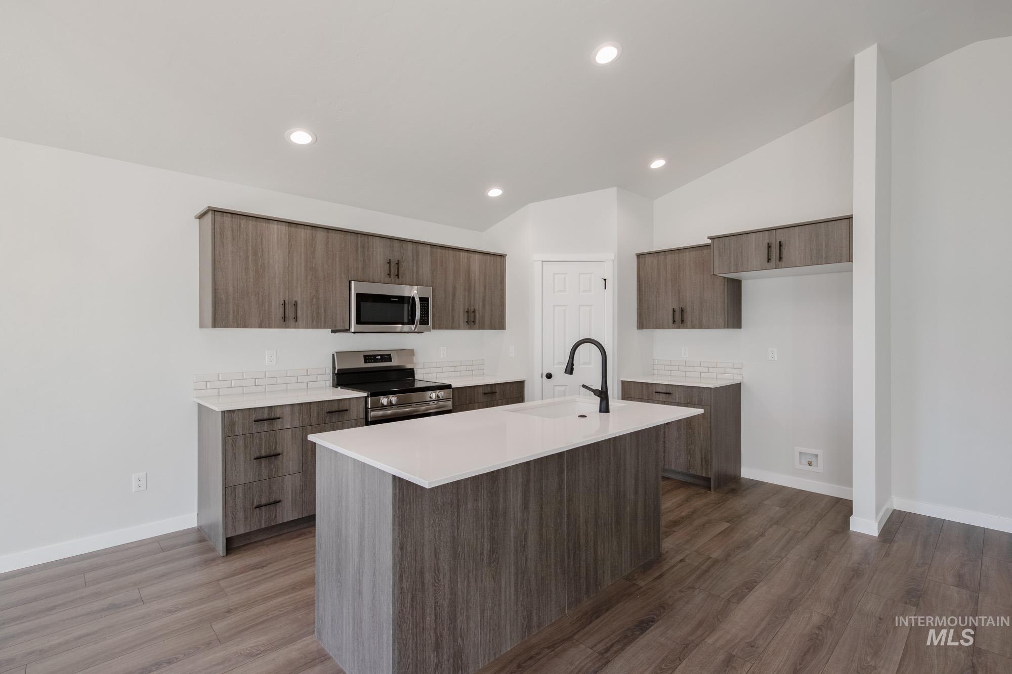 Kitchen featuring appliances with stainless steel finishes, vaulted ceiling, dark wood-style flooring, recessed lighting, and a kitchen island with sink