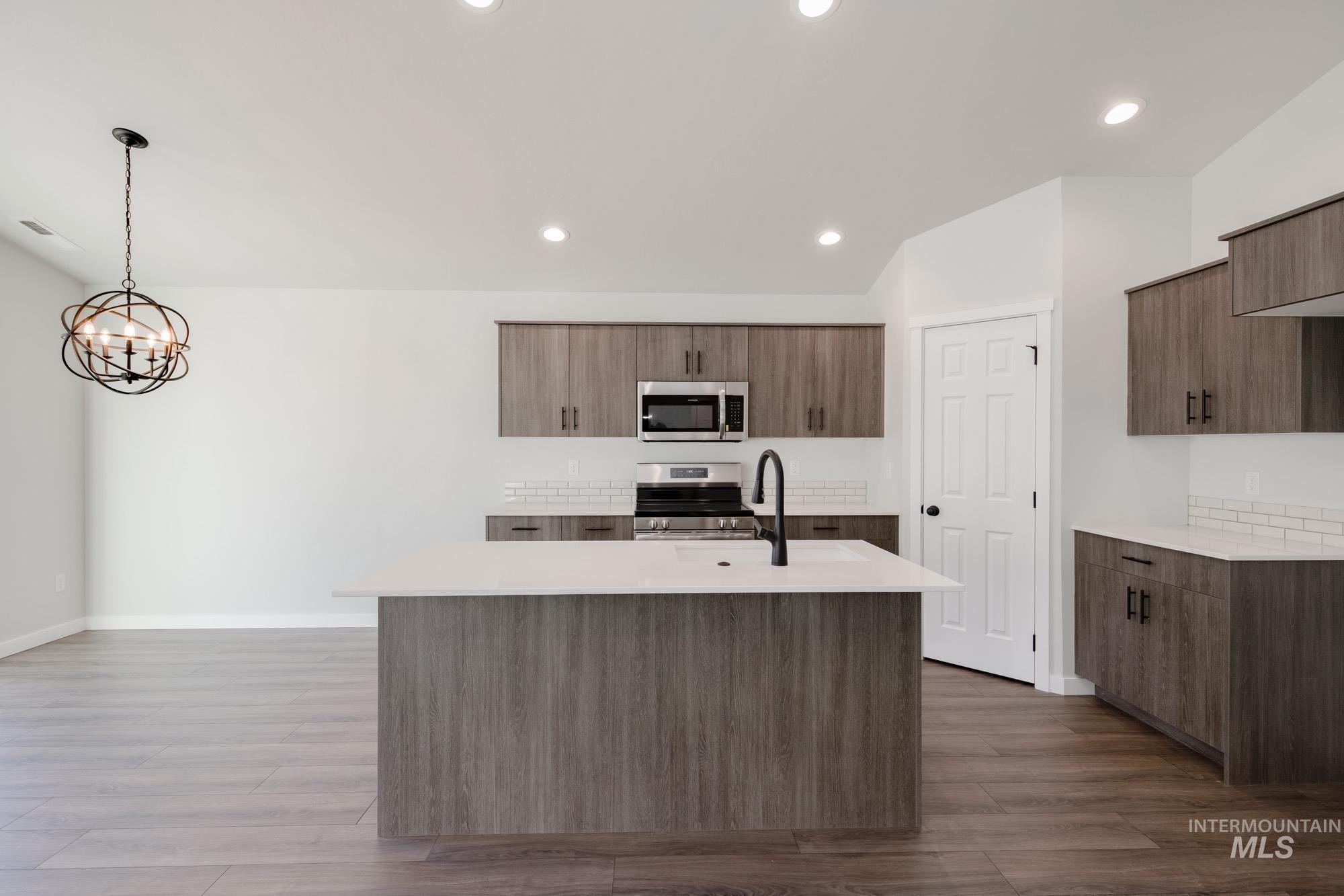 Kitchen featuring a center island with sink, decorative light fixtures, stainless steel appliances, recessed lighting, and dark wood-style flooring