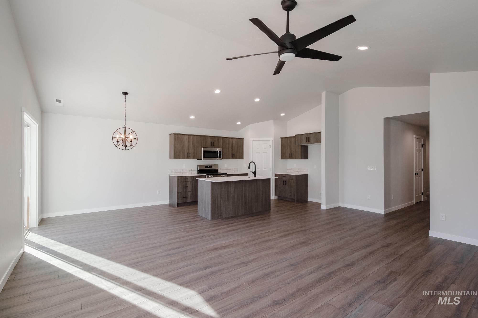Kitchen featuring open floor plan, vaulted ceiling, light countertops, recessed lighting, and dark wood-style flooring
