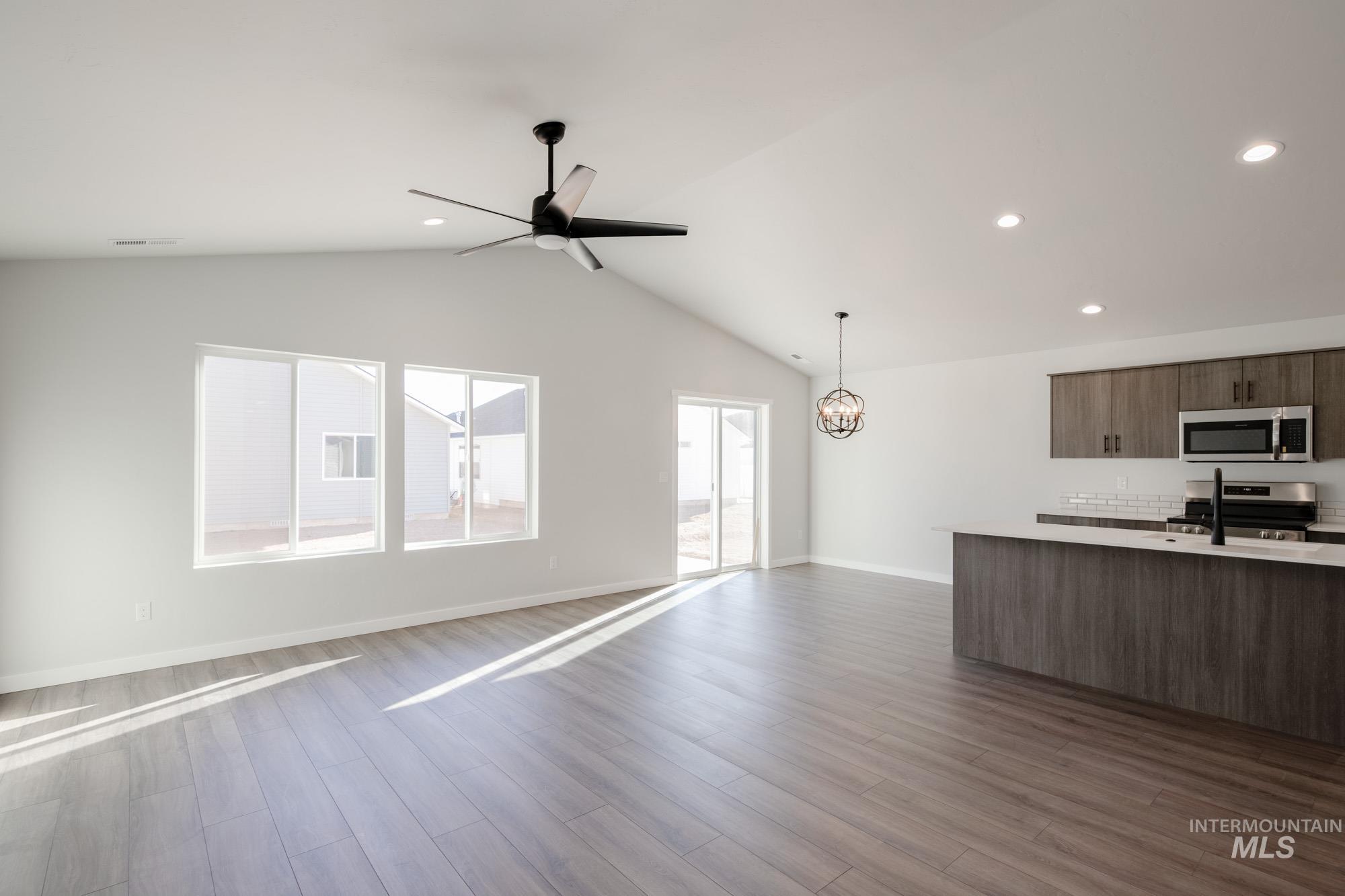 Kitchen featuring open floor plan, stainless steel appliances, dark wood finished floors, hanging light fixtures, and vaulted ceiling