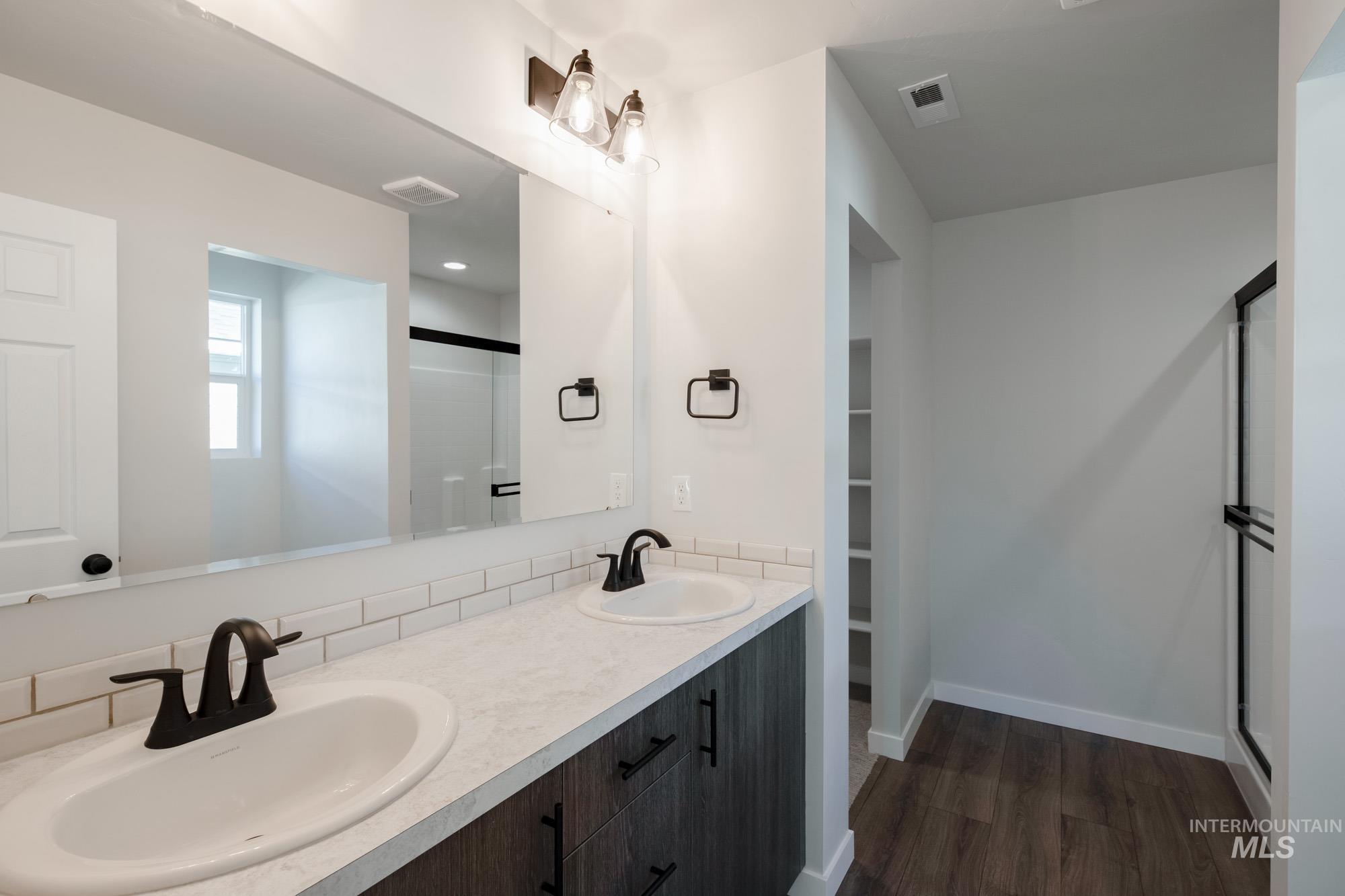 Full bathroom featuring a stall shower, double vanity, dark wood finished floors, and a walk in closet