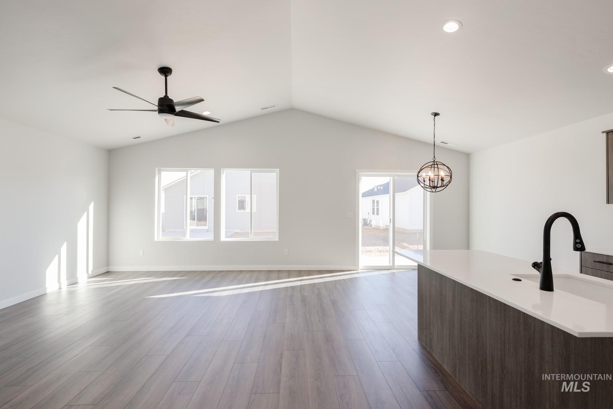 Unfurnished living room with dark wood finished floors, a ceiling fan, a chandelier, recessed lighting, and lofted ceiling