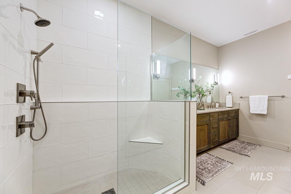 Primary bath with a glass & tile walk-in shower, vanity, and light tile patterned floors