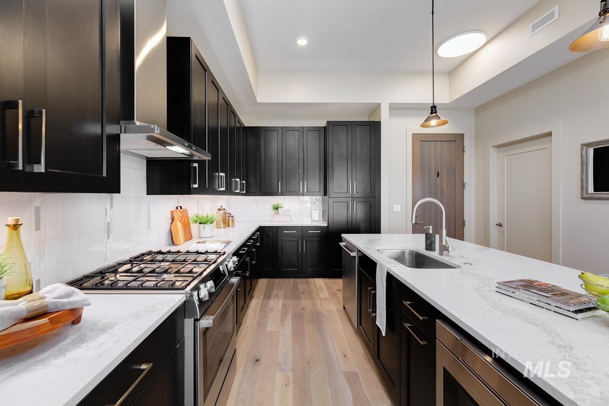 Kitchen featuring dark cabinets, appliances with stainless steel finishes, decorative backsplash, light stone counters, and recessed lighting
