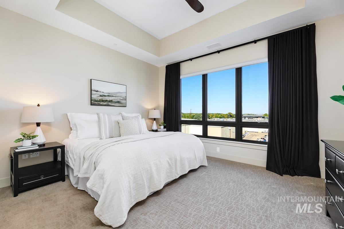 Bedroom with a tray ceiling, light colored carpet, and a ceiling fan