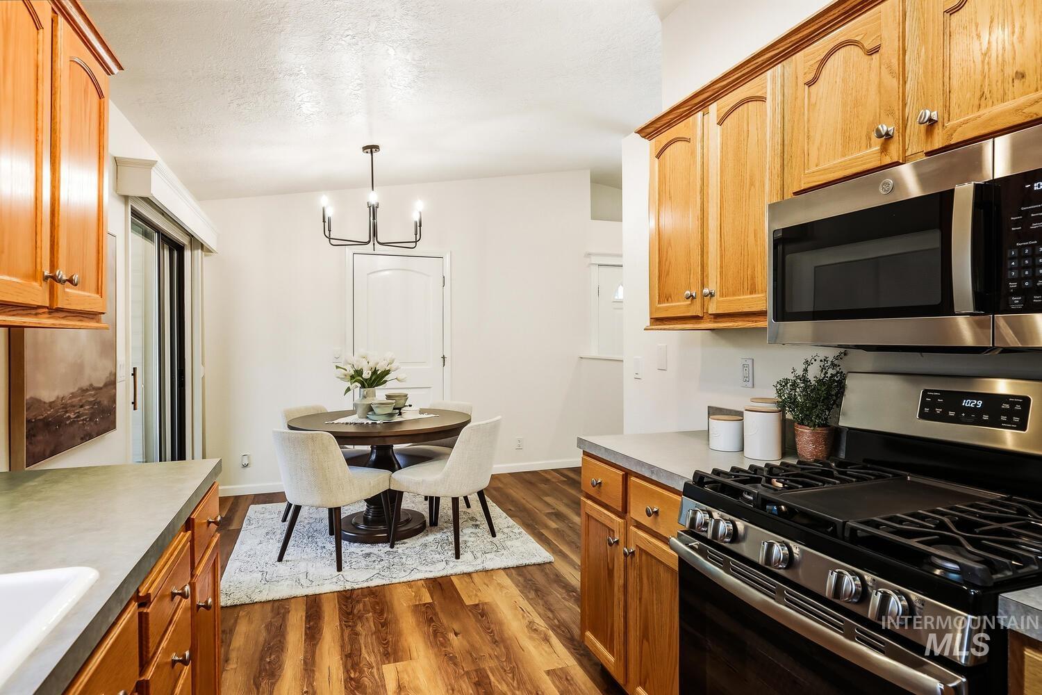Kitchen with stainless steel appliances, dark wood finished floors, suspended lighting, wood finish cabinetry, and a textured ceiling