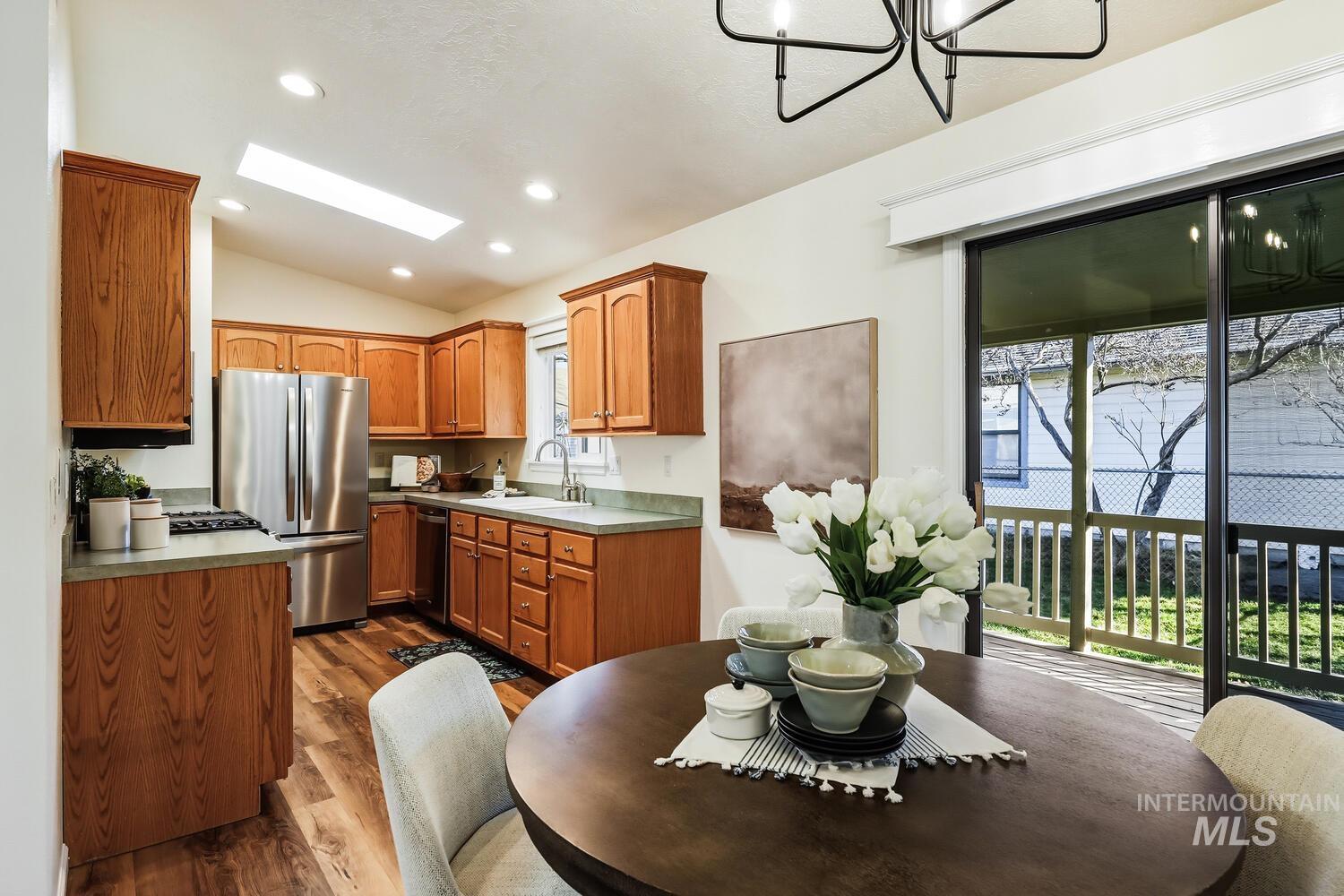 Kitchen with stainless steel appliances, dark wood-style floors, wood finish cabinetry, vaulted ceiling, and a chandelier
