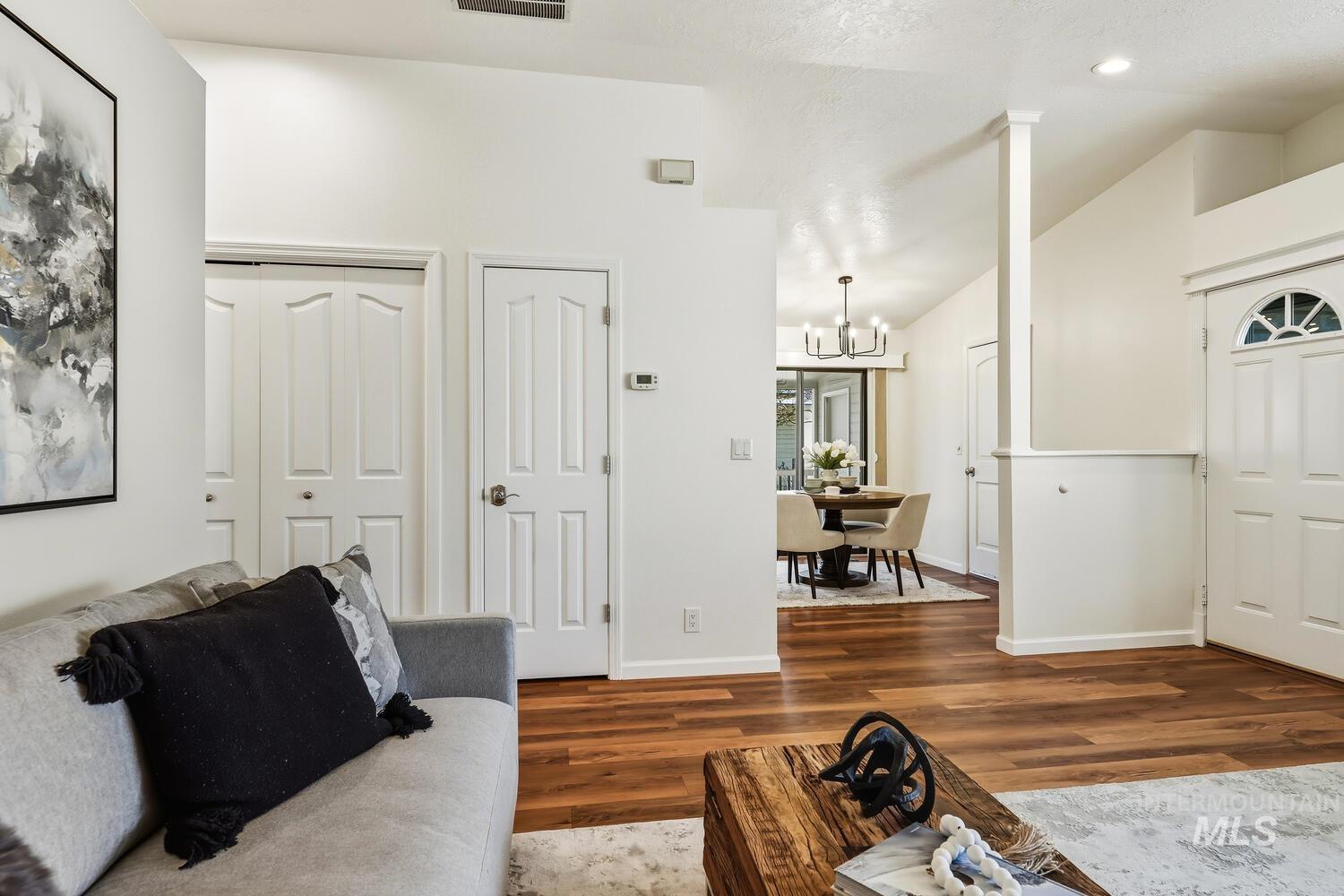 Living room with wood finished floors, hanging lights, and lofted ceiling