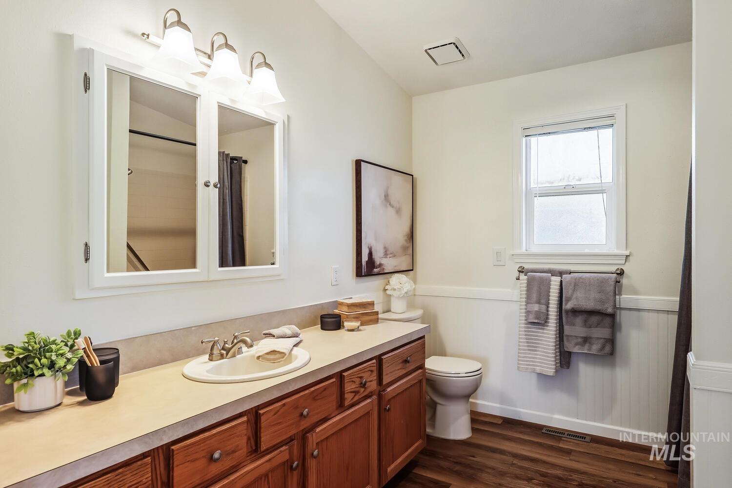 Full bath with vanity, a wainscoted wall, a shower with shower curtain, and dark wood-type flooring