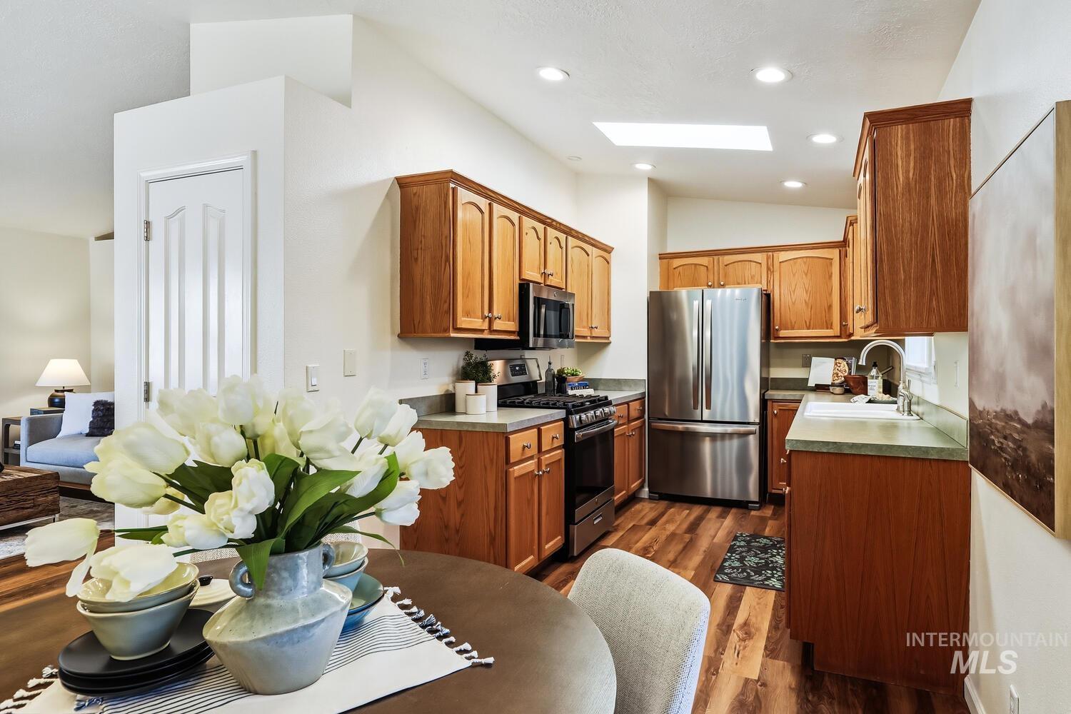 Kitchen with a skylight, stainless steel appliances, dark wood-style flooring, lofted ceiling, and wood finish cabinets