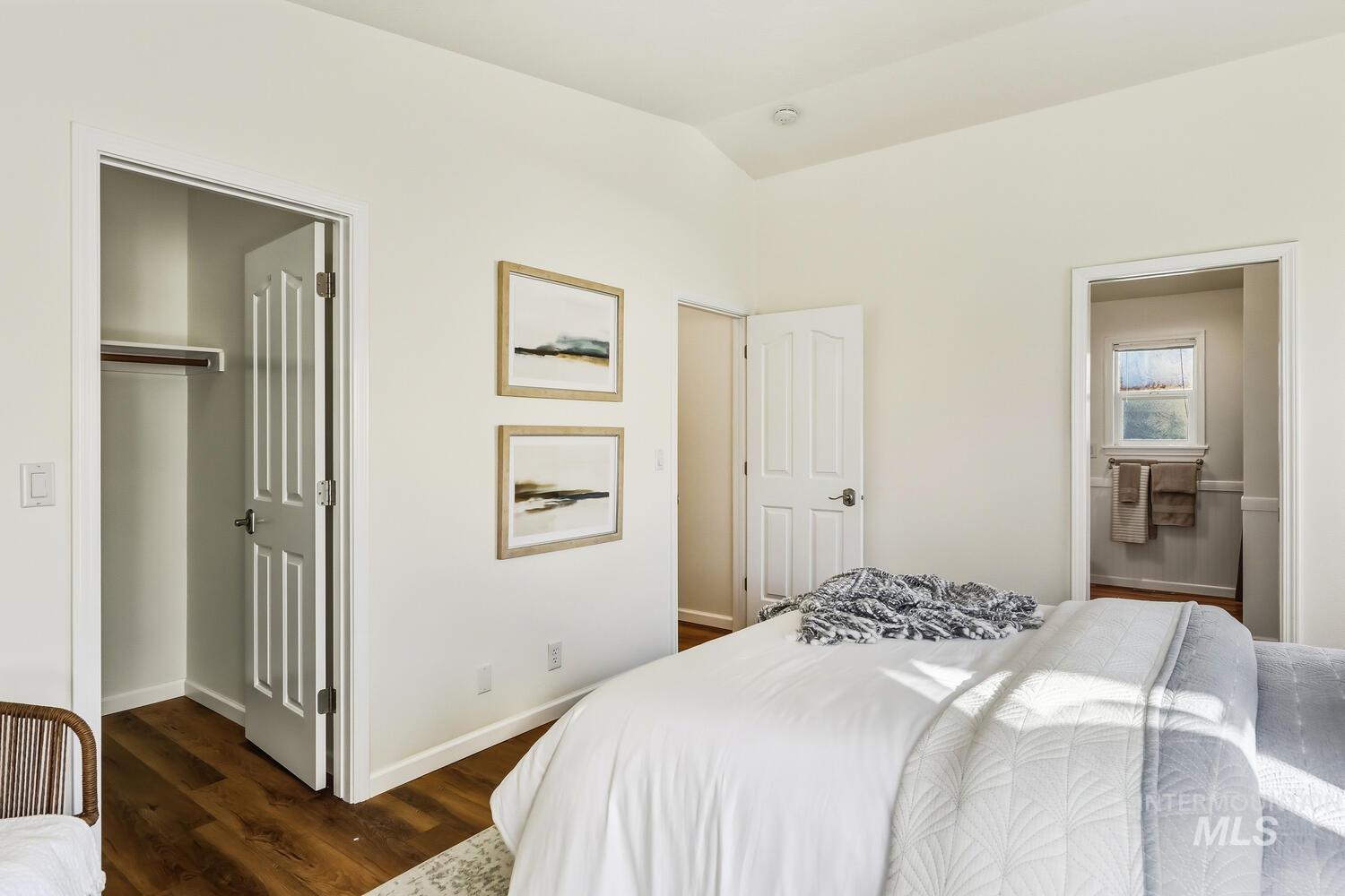 Bedroom with ensuite bathroom, dark wood-style flooring, lofted ceiling, and a spacious closet