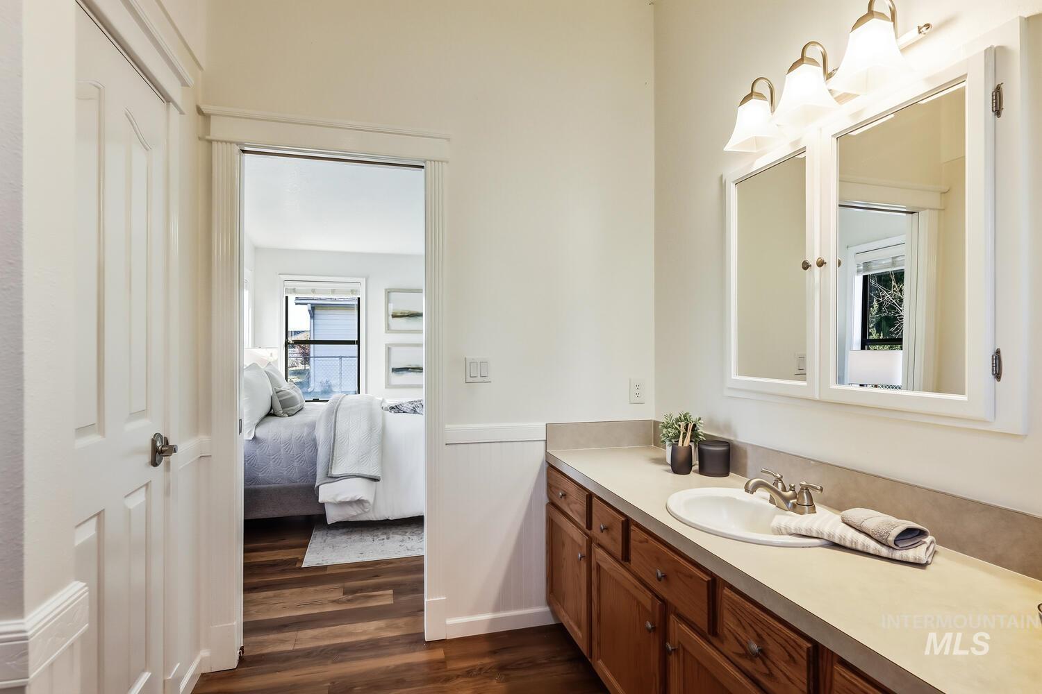 Ensuite bathroom with vanity, a wainscoted wall, and dark wood-type flooring