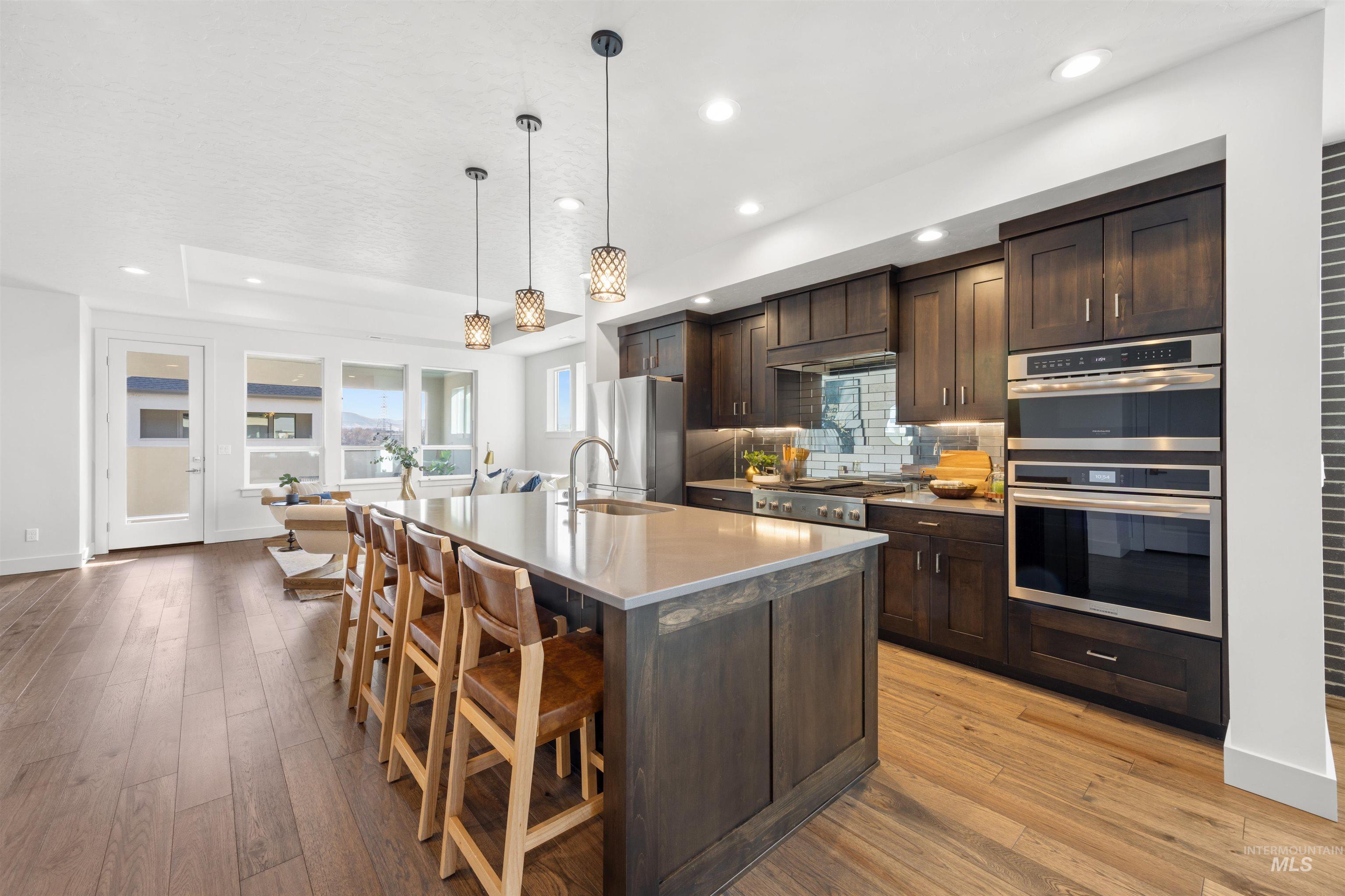 Kitchen with dark wood finish cabinets, backsplash, a kitchen breakfast bar, a kitchen island with sink, and light wood-type flooring