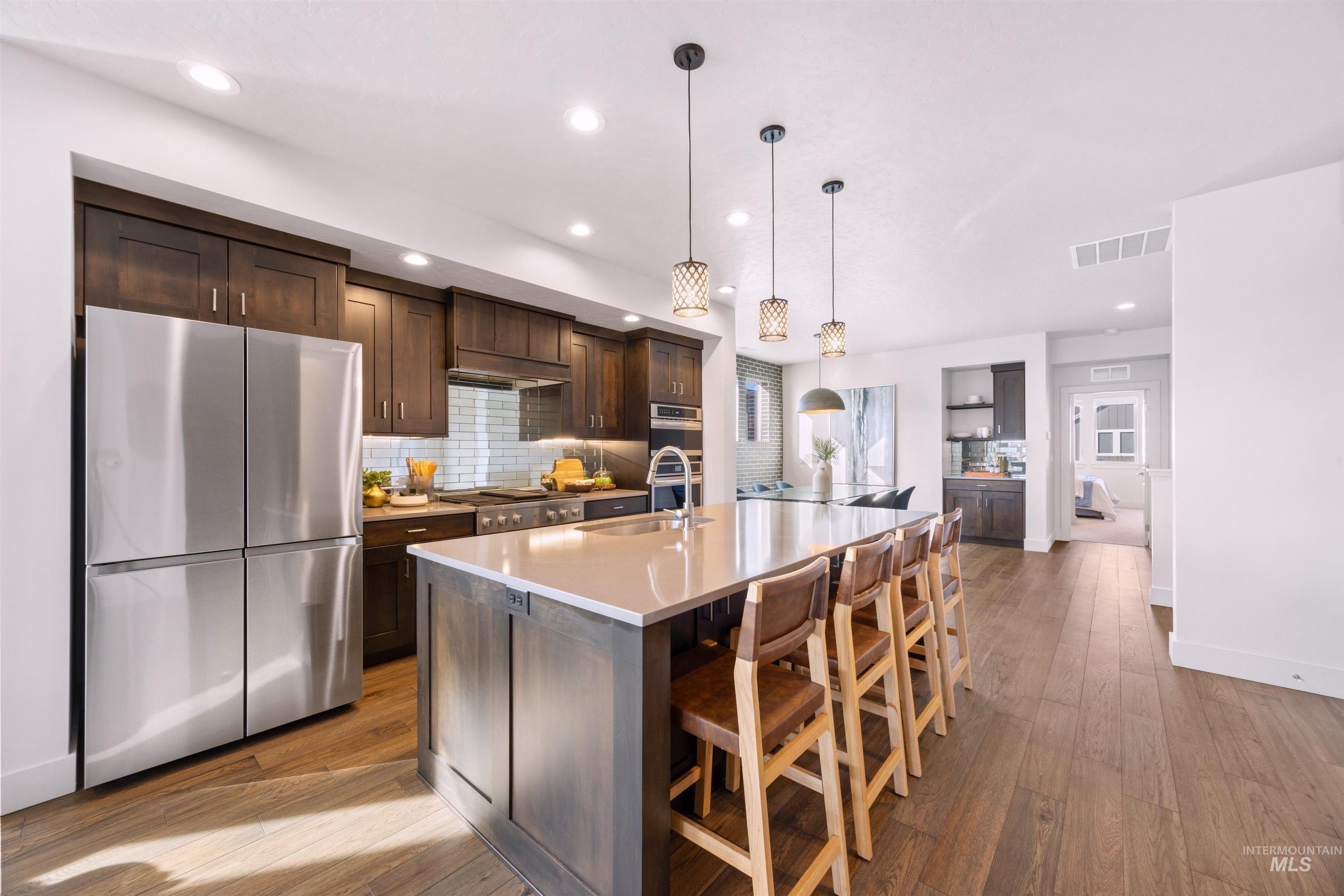 Kitchen with stainless steel appliances, backsplash, dark wood finish cabinetry, light wood-type flooring, and a kitchen bar