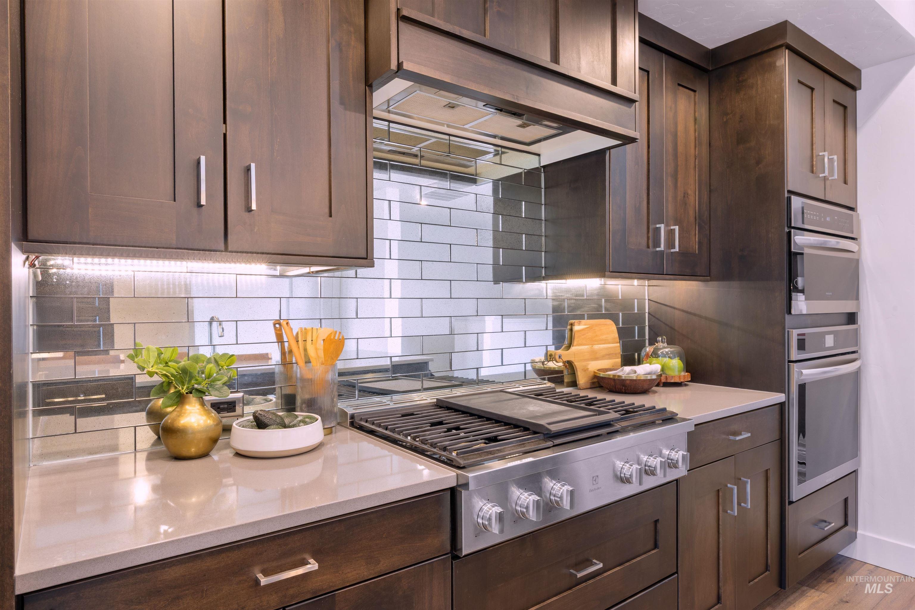 Kitchen with dark wood finish cabinets, extractor fan, stainless steel appliances, decorative backsplash, and light stone counters