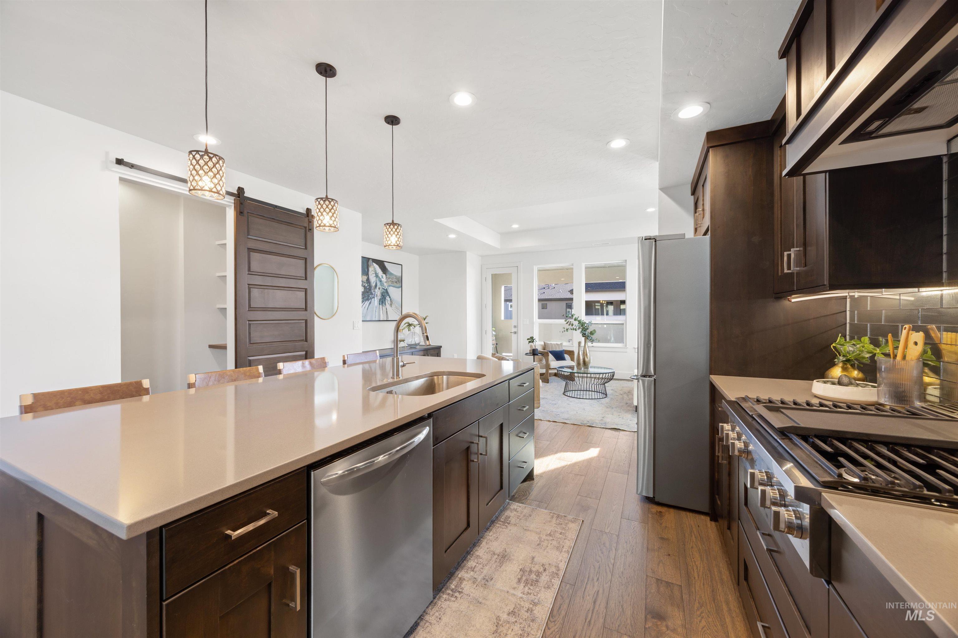 Kitchen featuring dark wood finish cabinets, stainless steel appliances, extractor fan, hanging light fixtures, and dark wood-style floors