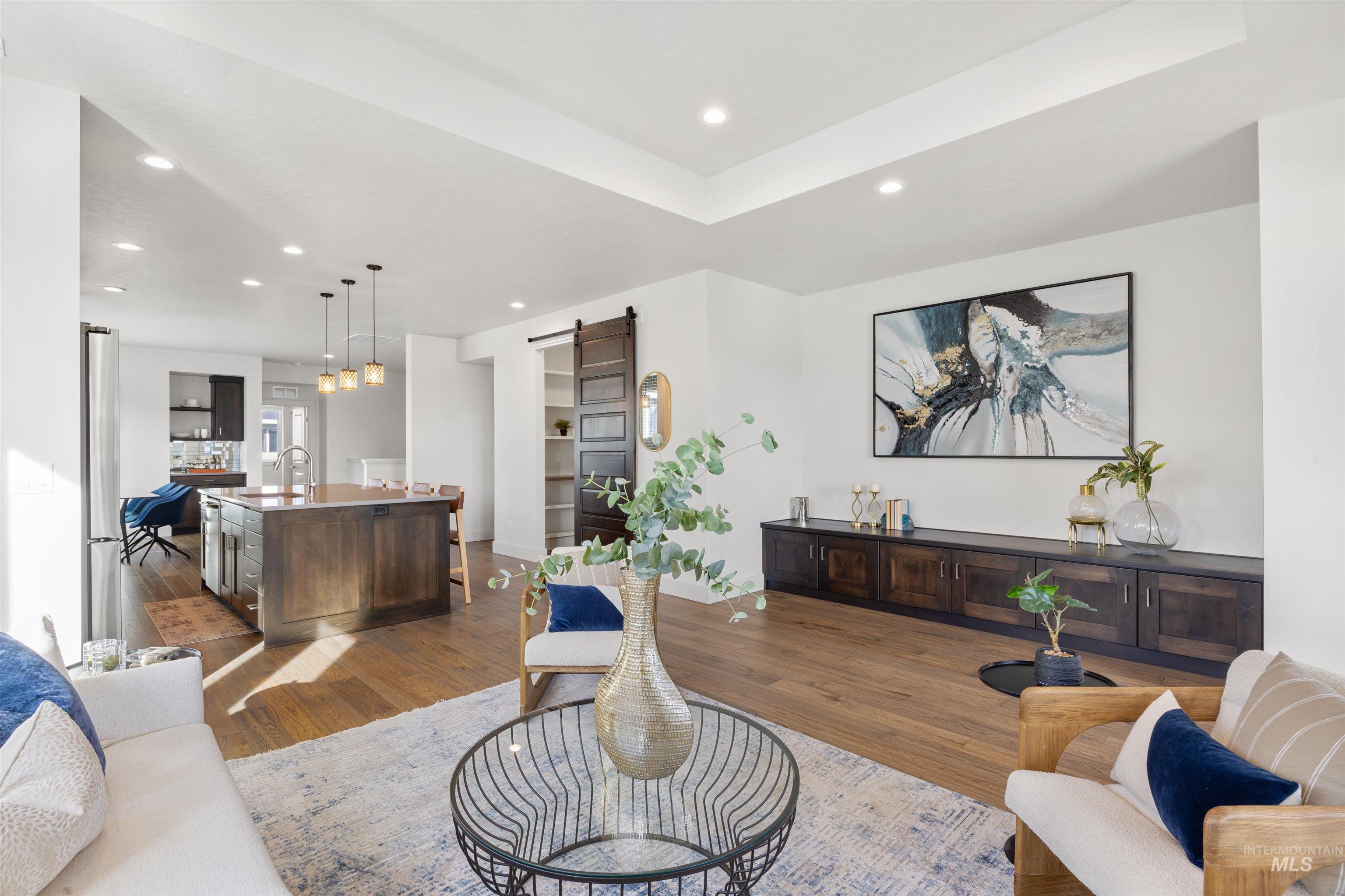 Living area featuring a barn door, dark wood finished floors, recessed lighting, and a tray ceiling