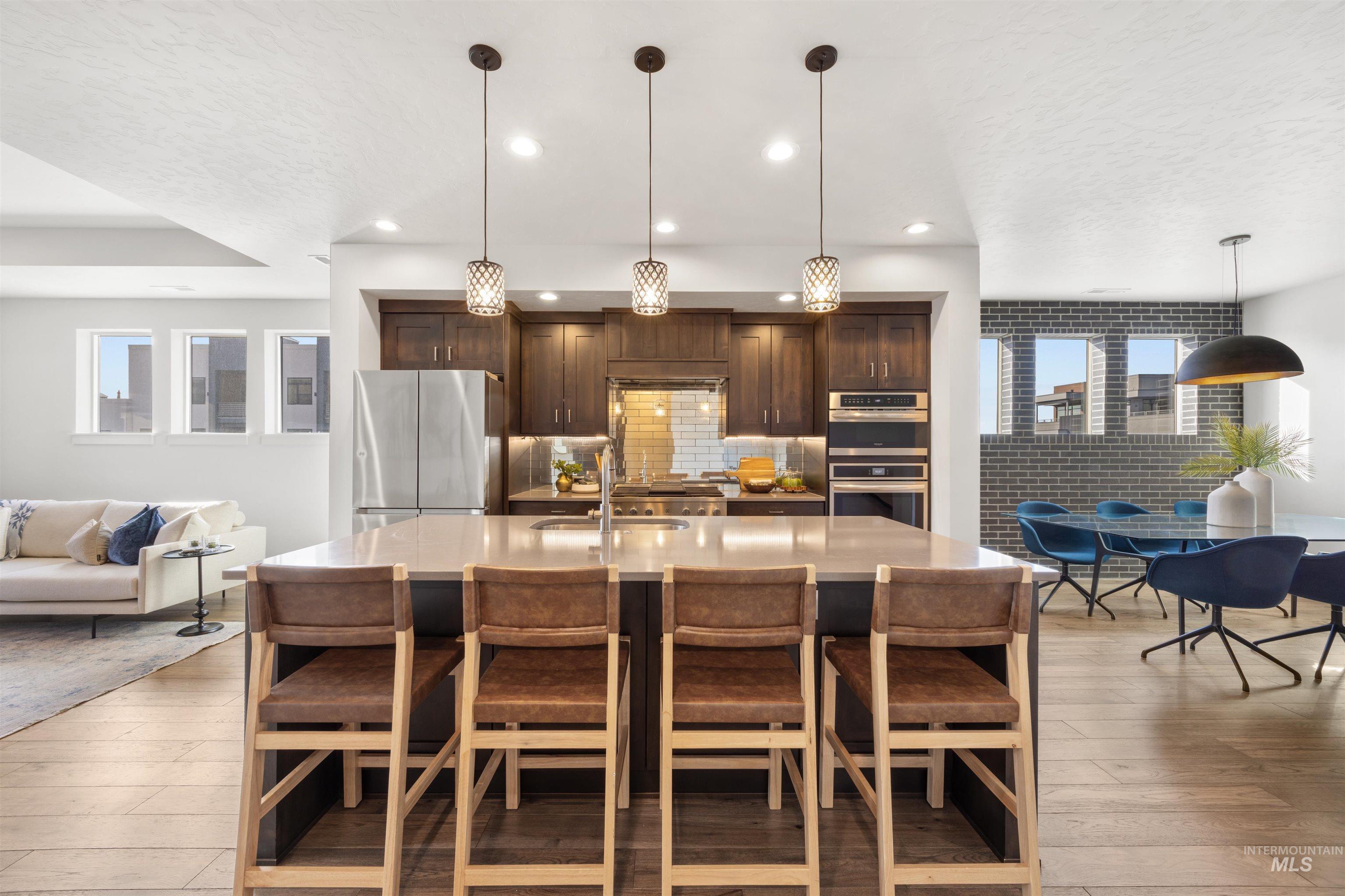 Kitchen with dark wood finish cabinetry, pendant lighting, open floor plan, stainless steel appliances, and a textured ceiling