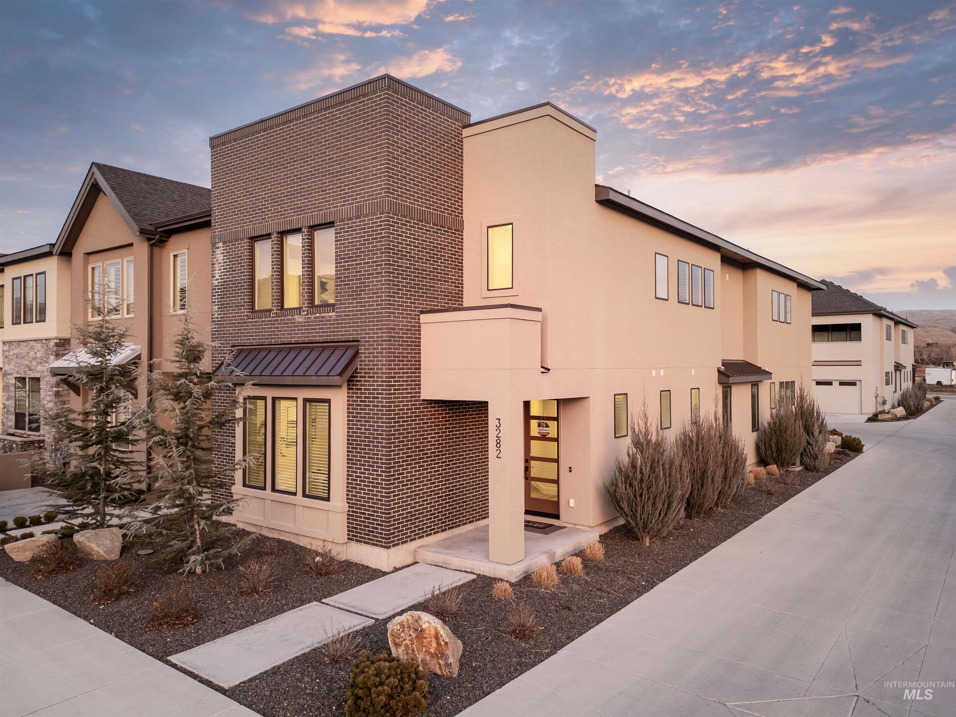View of front of property featuring brick siding, concrete driveway, stucco siding, and a standing seam roof