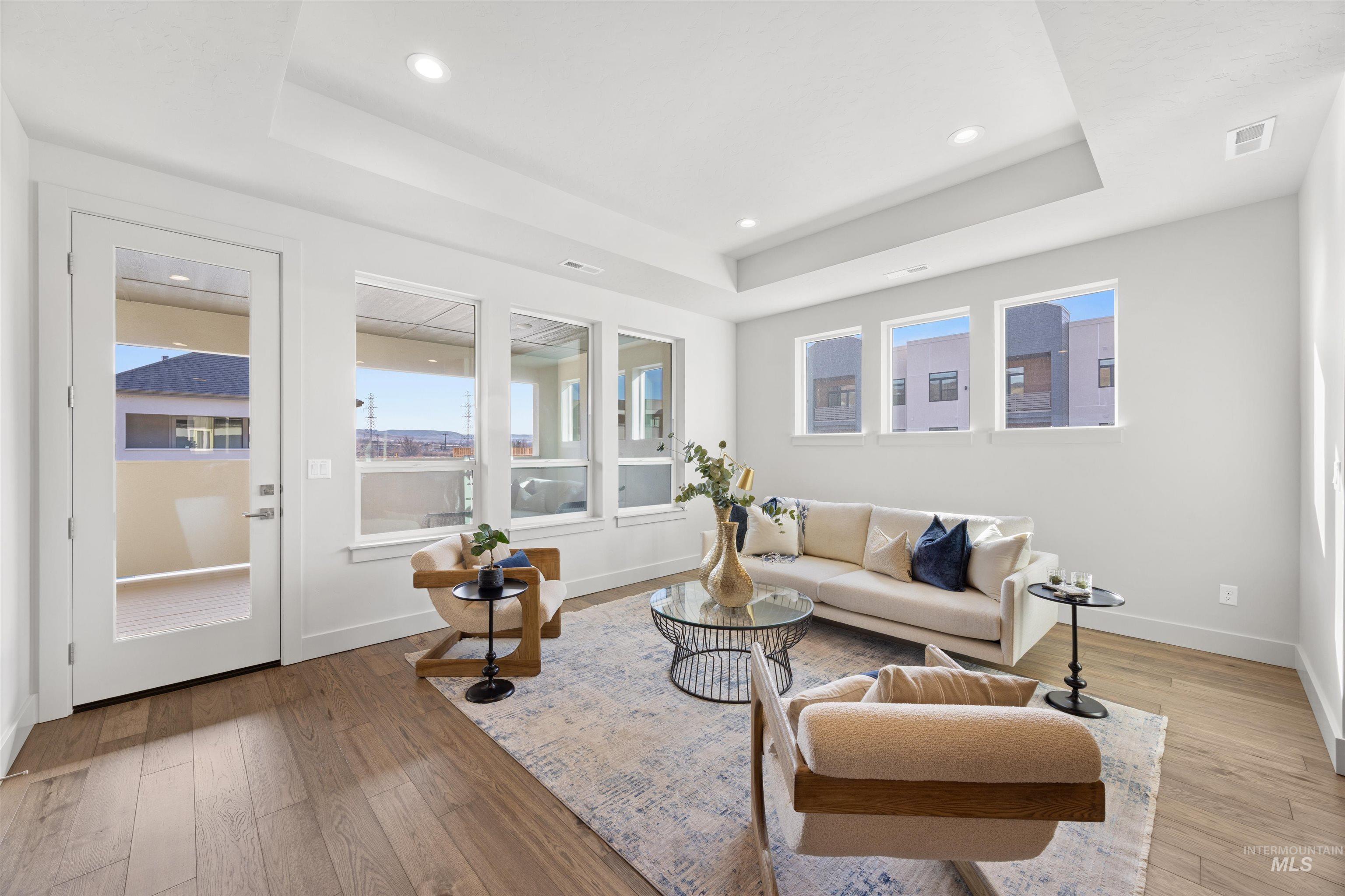 Living area with a raised ceiling, light wood-type flooring, and recessed lighting