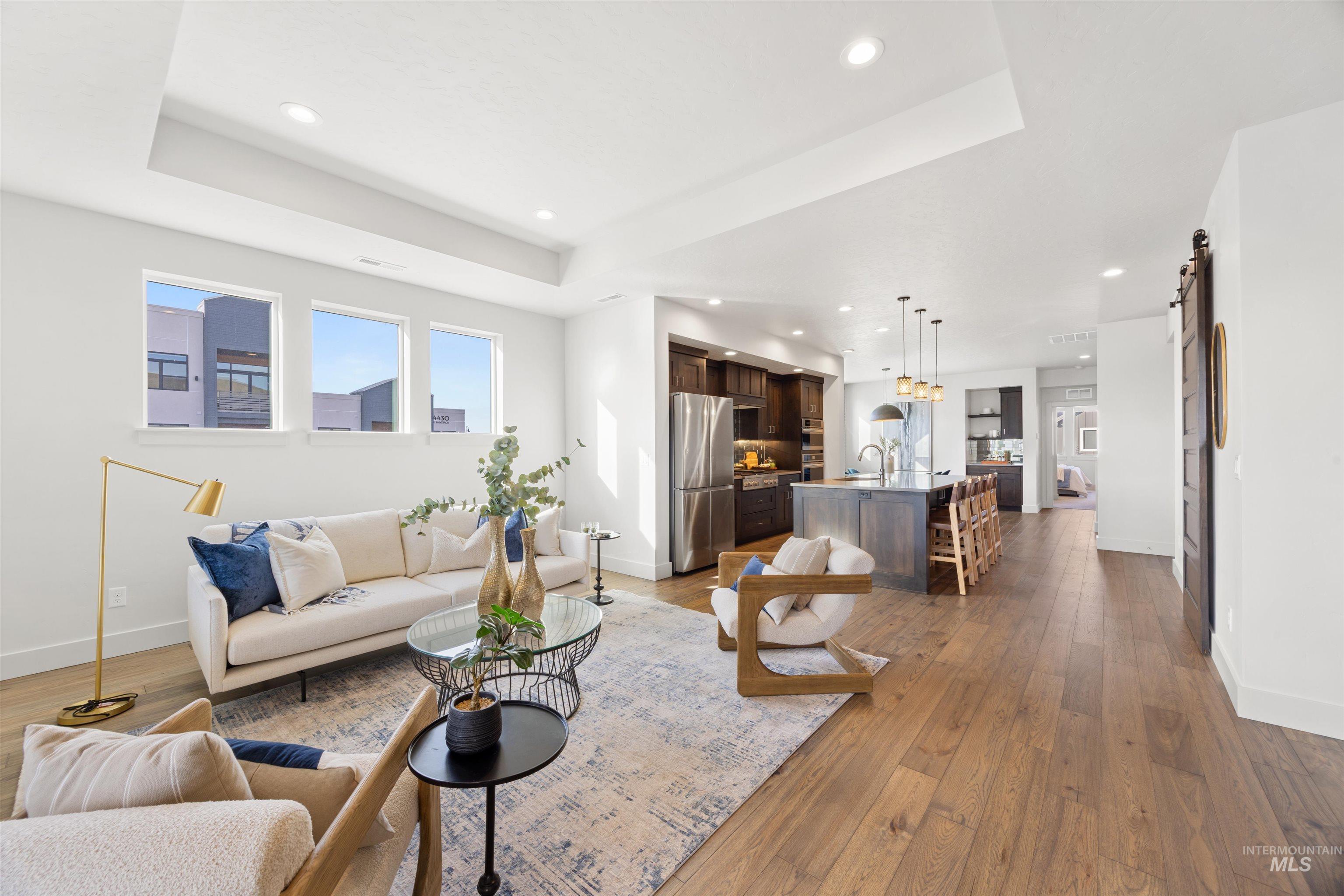 Living area featuring light wood-type flooring, a barn door, a raised ceiling, and recessed lighting