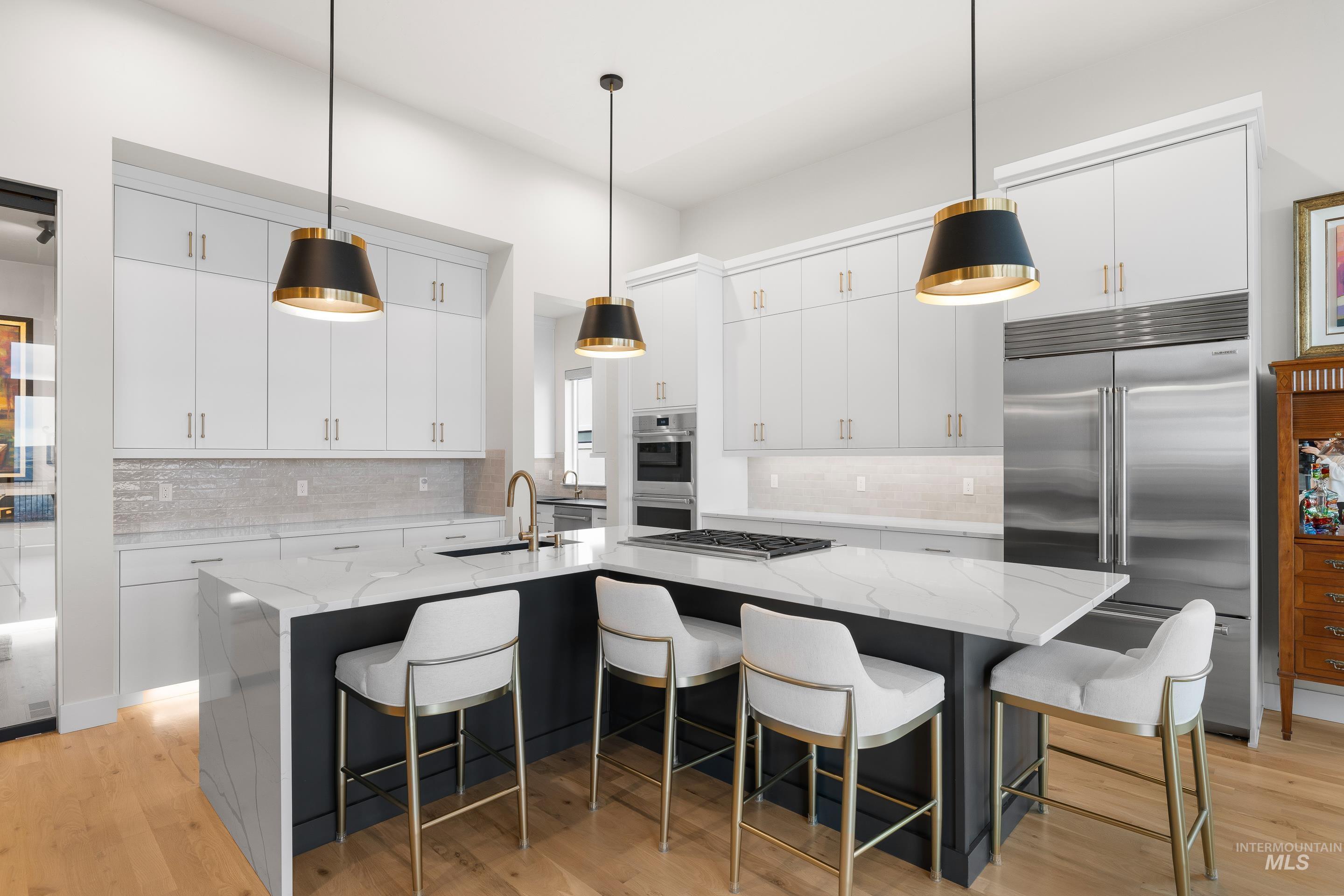 Dual tone kitchen featuring a kitchen bar, pendant lighting, light stone counters, stainless steel appliances, and two tone cabinets