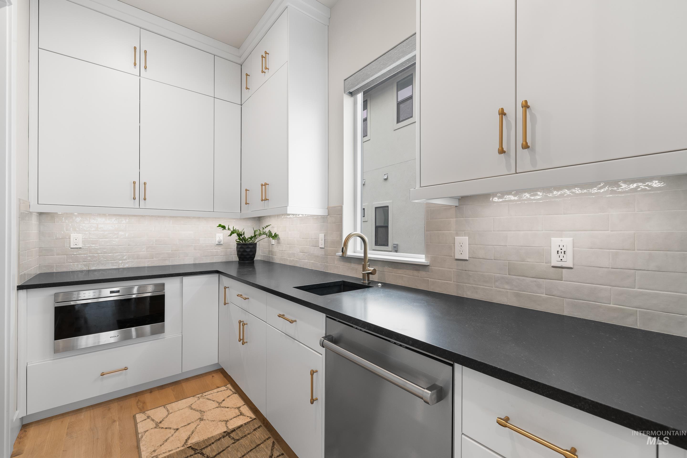 Kitchen featuring stainless steel appliances, light wood-type flooring, white cabinets, backsplash, and dark stone counters