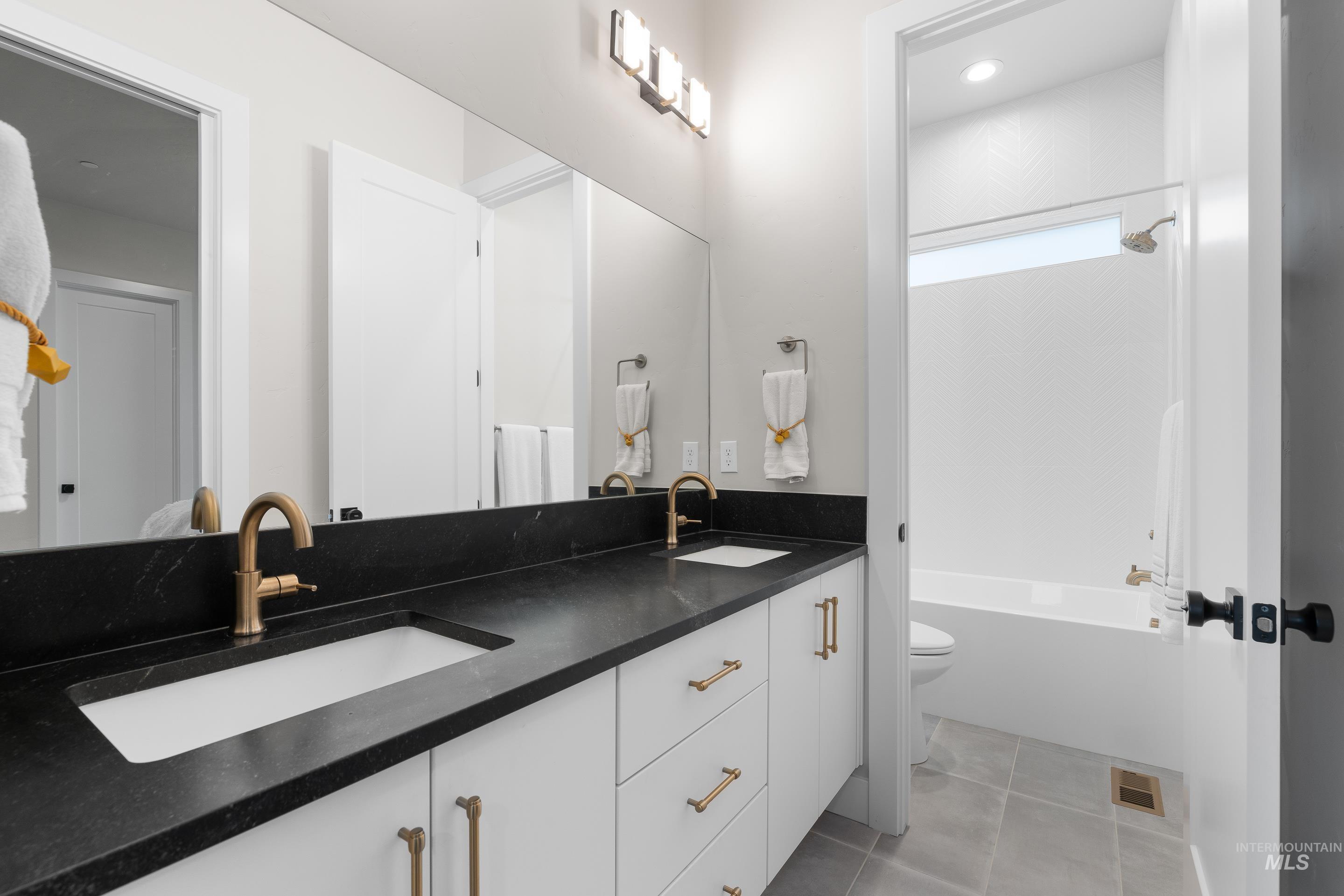 Bathroom with double vanity, tub / shower combination, light tile patterned floors, and recessed lighting