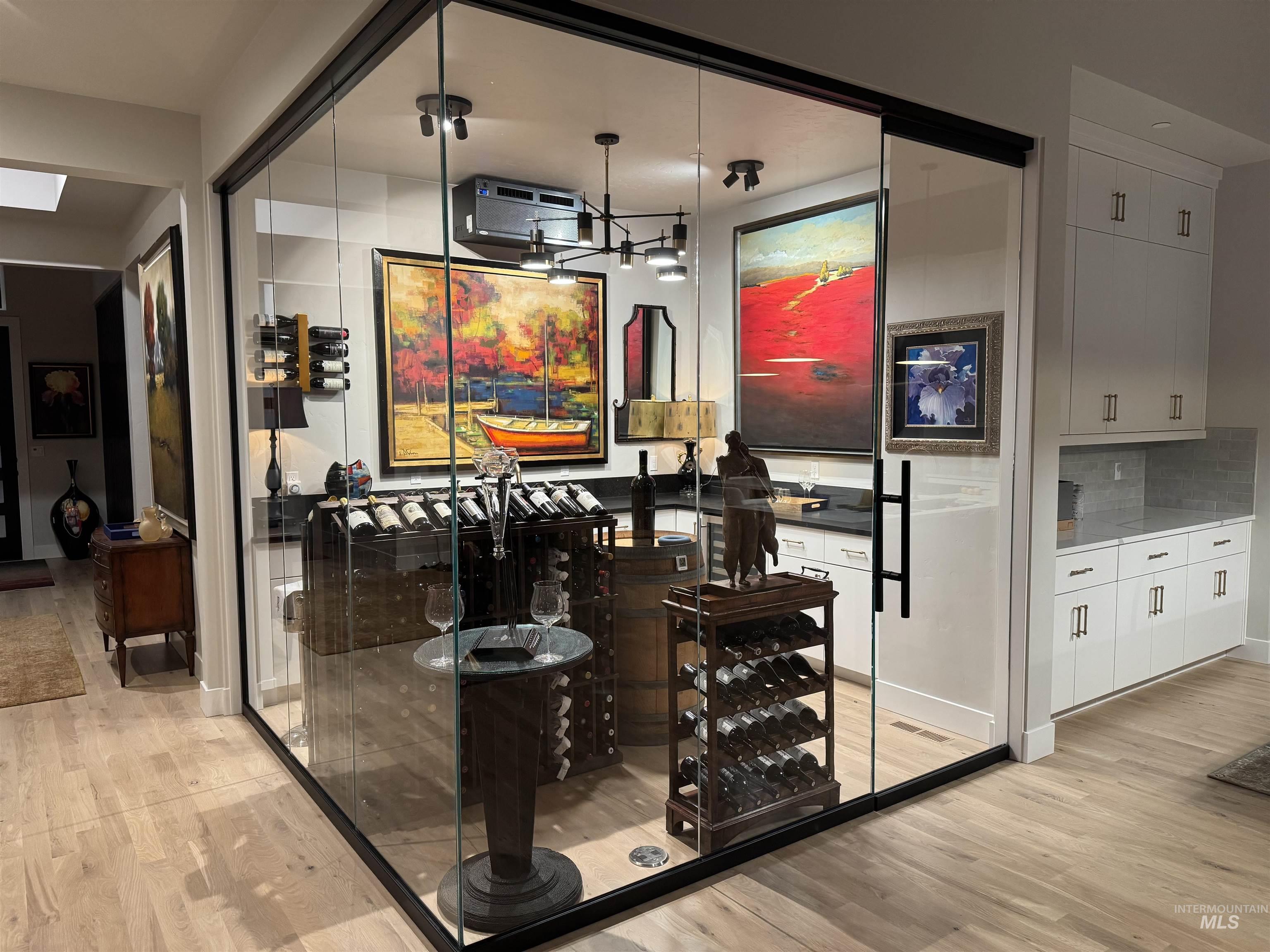 Bar with white cabinets, light wood-style floors, dark countertops, and decorative backsplash