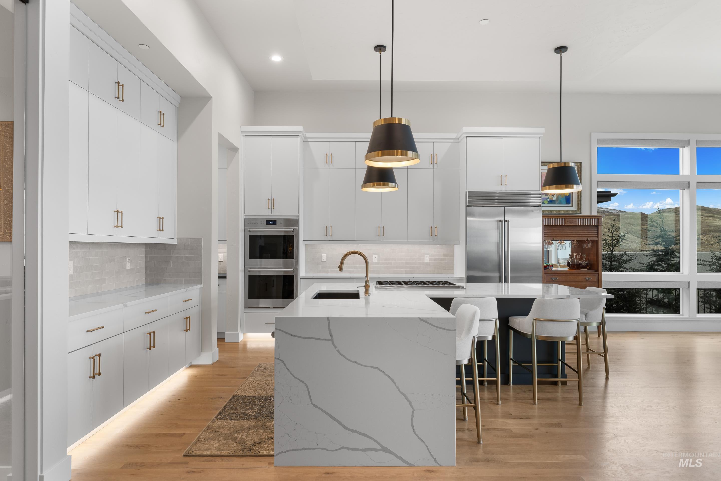 Kitchen featuring pendant lighting, light wood-style flooring, white cabinets, light stone countertops, and an island with sink