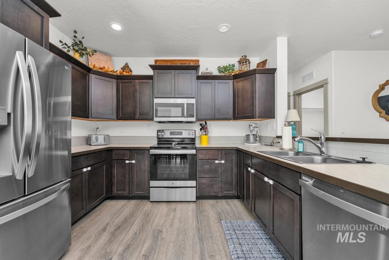 Kitchen featuring stainless steel appliances, dark brown cabinets, light wood-style flooring, a textured ceiling, and recessed lighting
