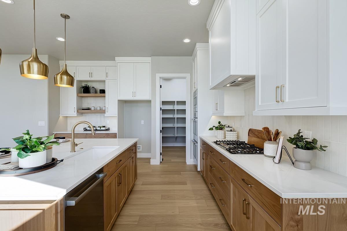 Kitchen with hanging light fixtures, brown cabinetry, white cabinets, appliances with stainless steel finishes, and light wood-type flooring