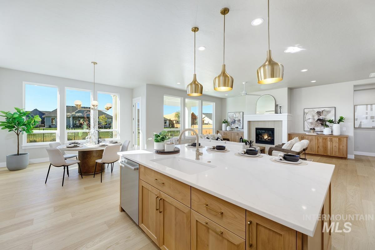 Kitchen featuring a fireplace, light wood-style floors, light brown cabinets, pendant lighting, and an island with sink
