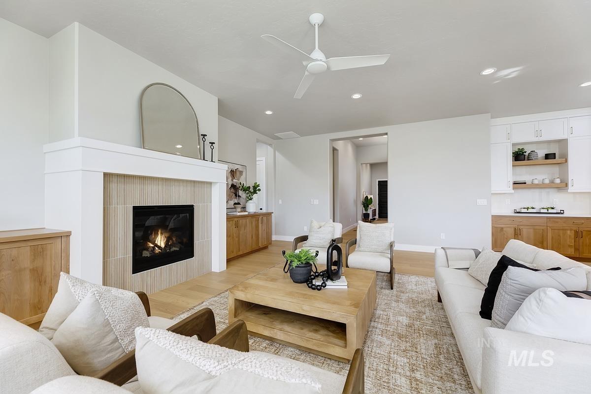 Living area featuring light wood-type flooring, a fireplace, ceiling fan, and recessed lighting