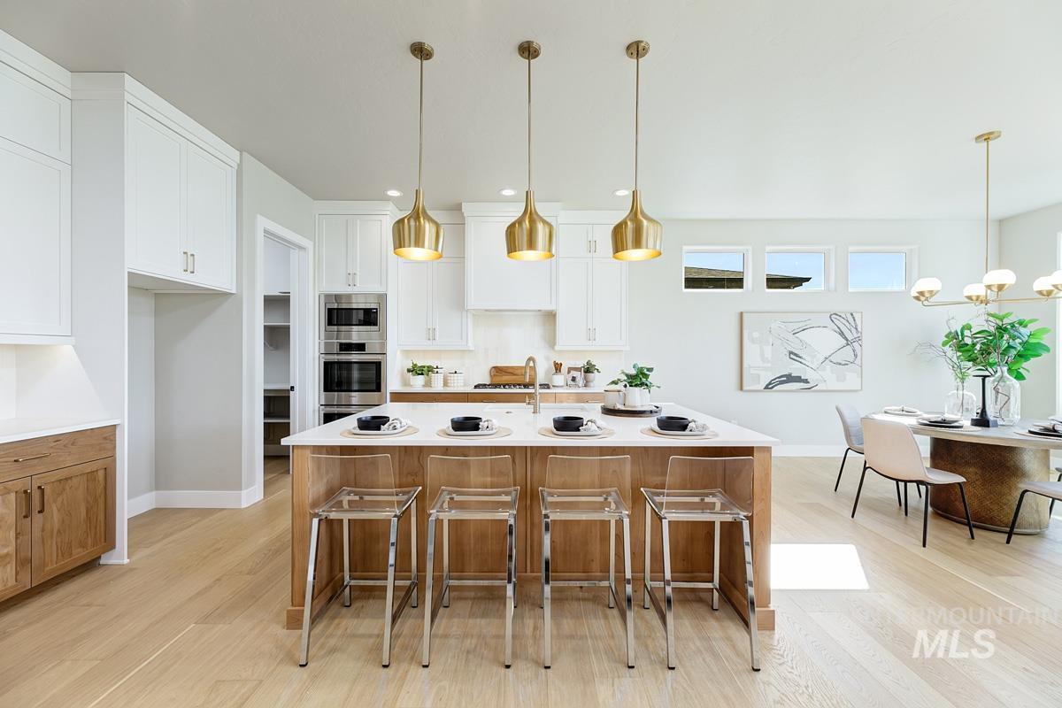 Kitchen with a breakfast bar, brown cabinetry, light wood-type flooring, white cabinets, and recessed lighting