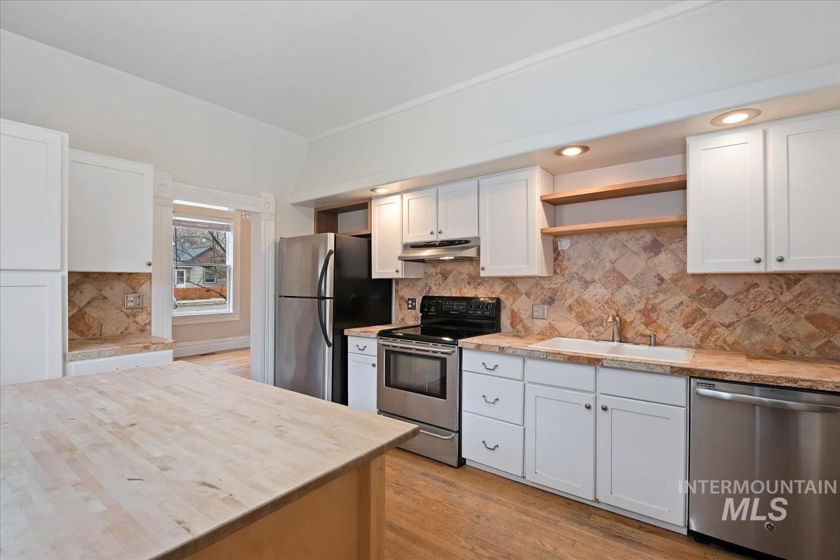 Kitchen with appliances with stainless steel finishes, butcher block countertops, light wood-style floors, white cabinets, and open shelves