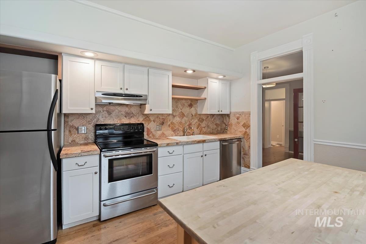 Kitchen featuring open shelves, appliances with stainless steel finishes, white cabinetry, light wood finished floors, and under cabinet range hood