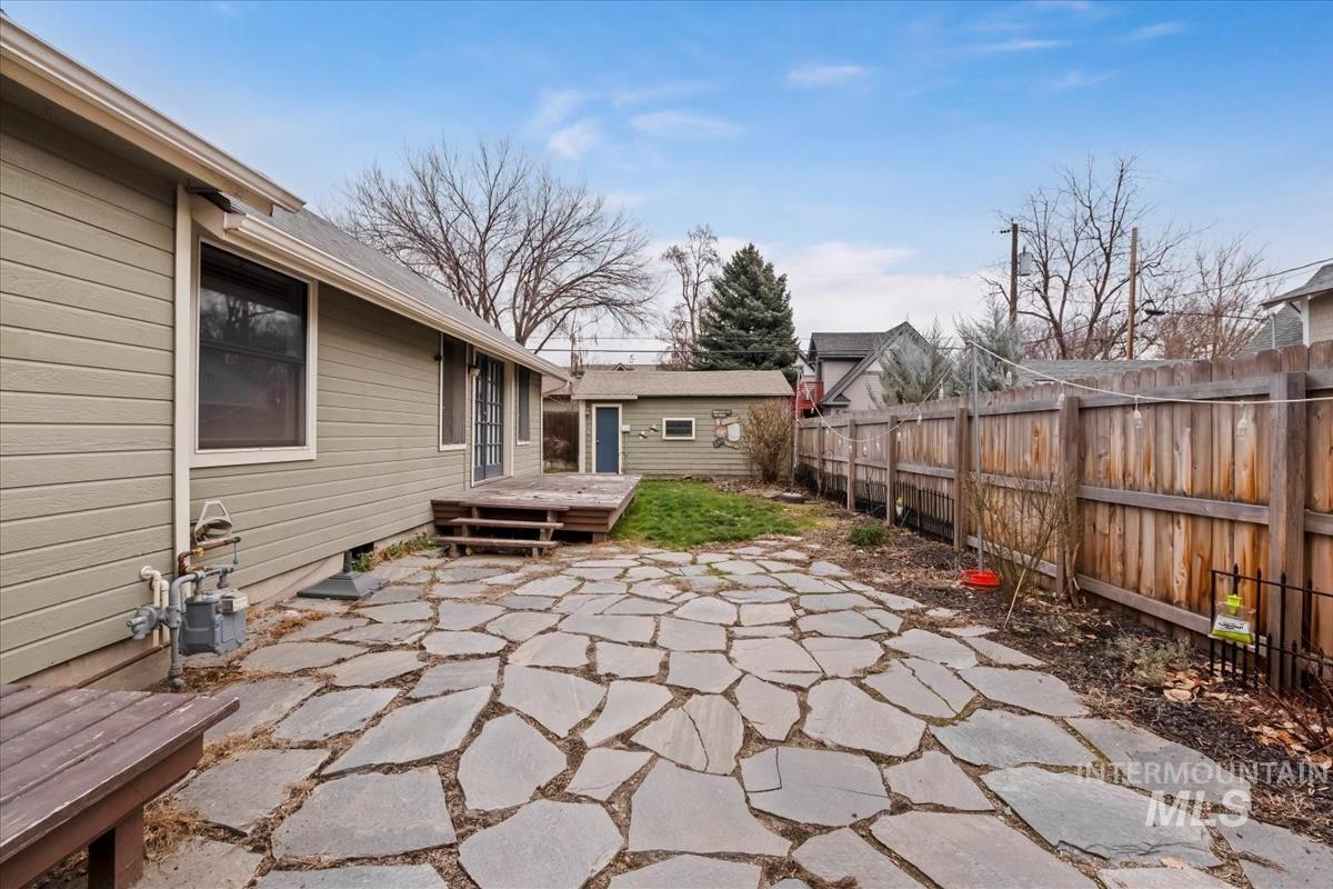 Fenced backyard with a wooden deck, a patio, and an outdoor structure
