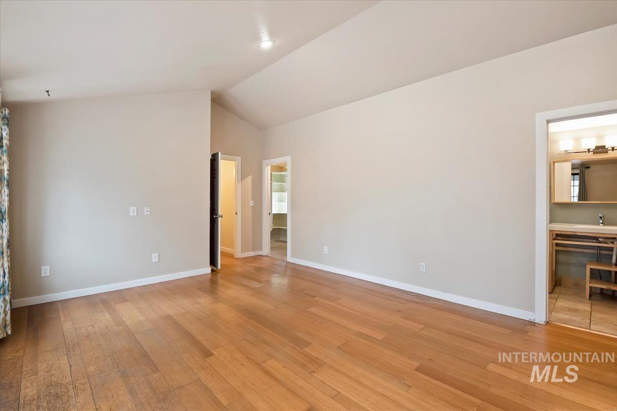 Unfurnished bedroom featuring light wood-style floors, lofted ceiling, and ensuite bath