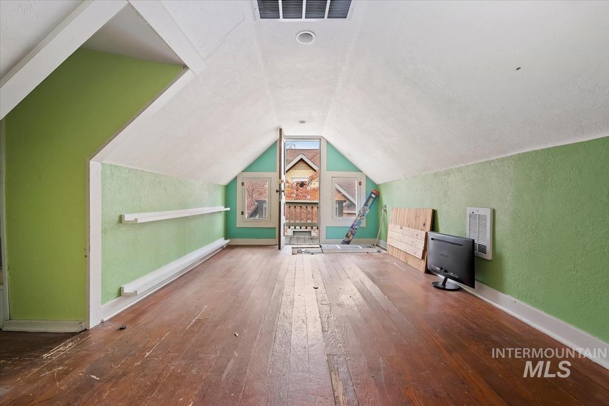 Additional living space featuring wood-type flooring, lofted ceiling, a baseboard radiator, and a textured wall