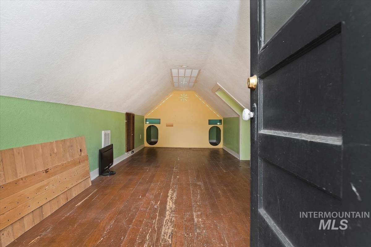 Bonus room with dark wood-type flooring, lofted ceiling, and a textured ceiling
