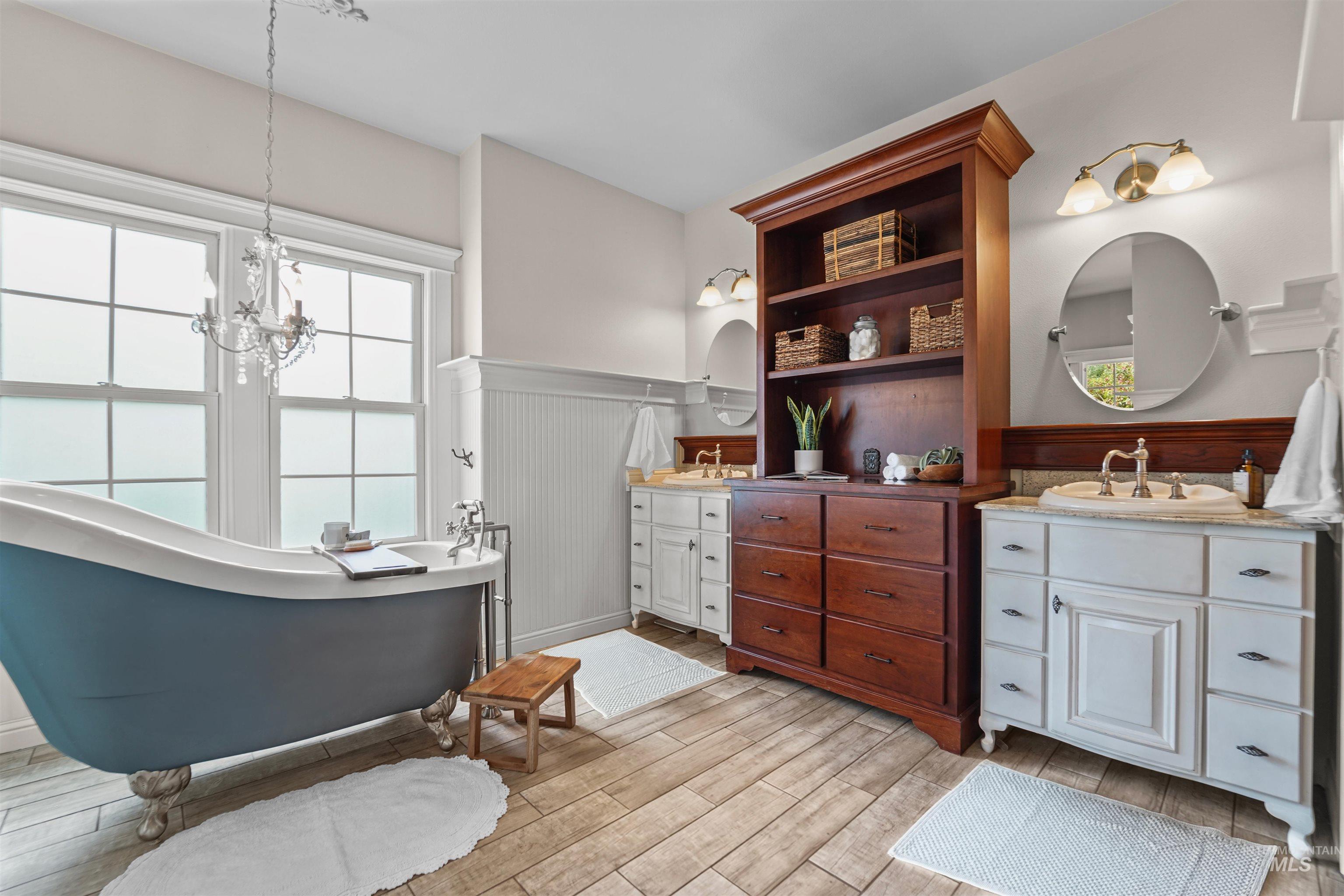 Bathroom featuring two vanities, wainscoting, a freestanding bath, wood finished floors, and a chandelier