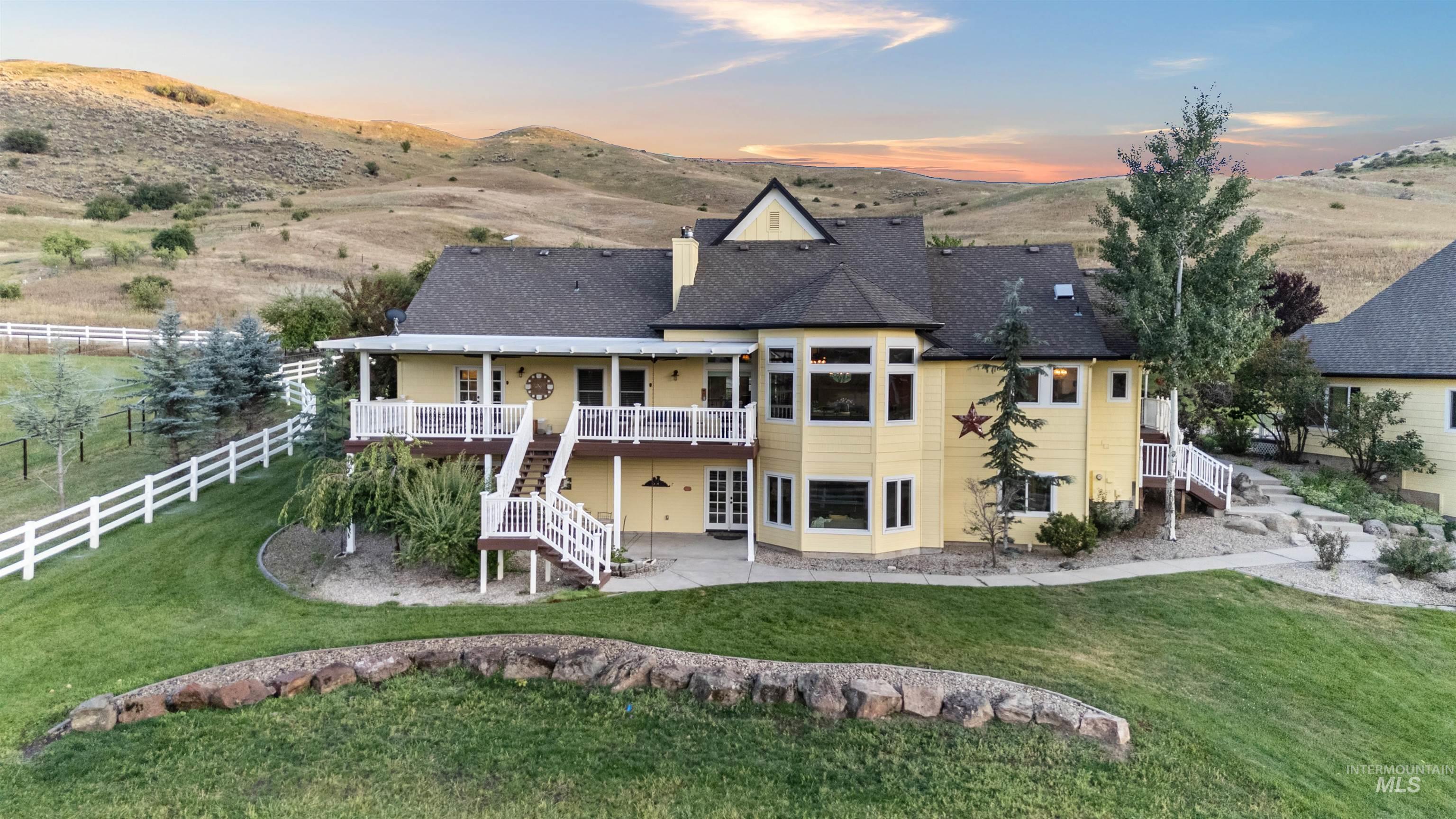 Back of property at dusk featuring stairs, a patio, a deck with mountain view, roof with shingles, and a chimney