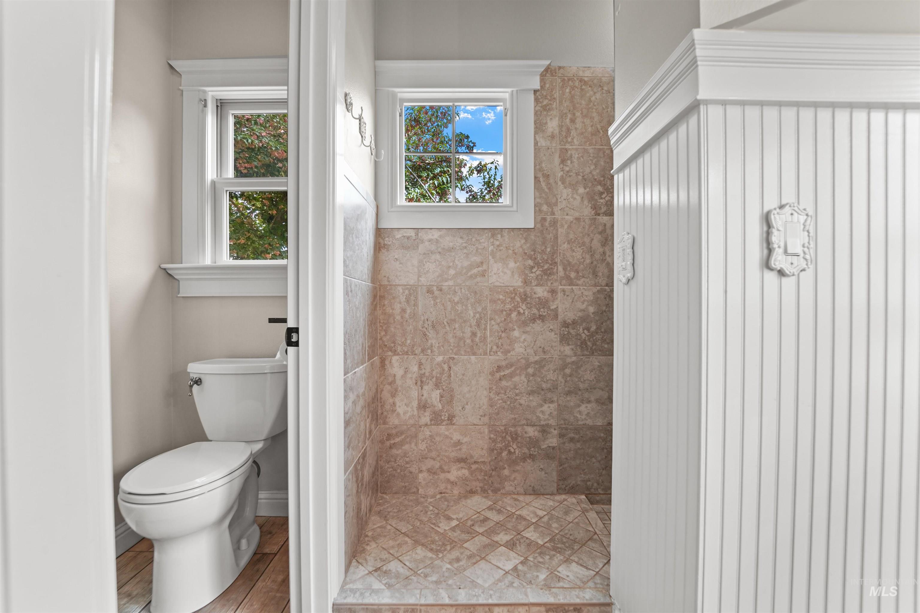 Full bath featuring healthy amount of natural light, tiled shower, and wood finished floors